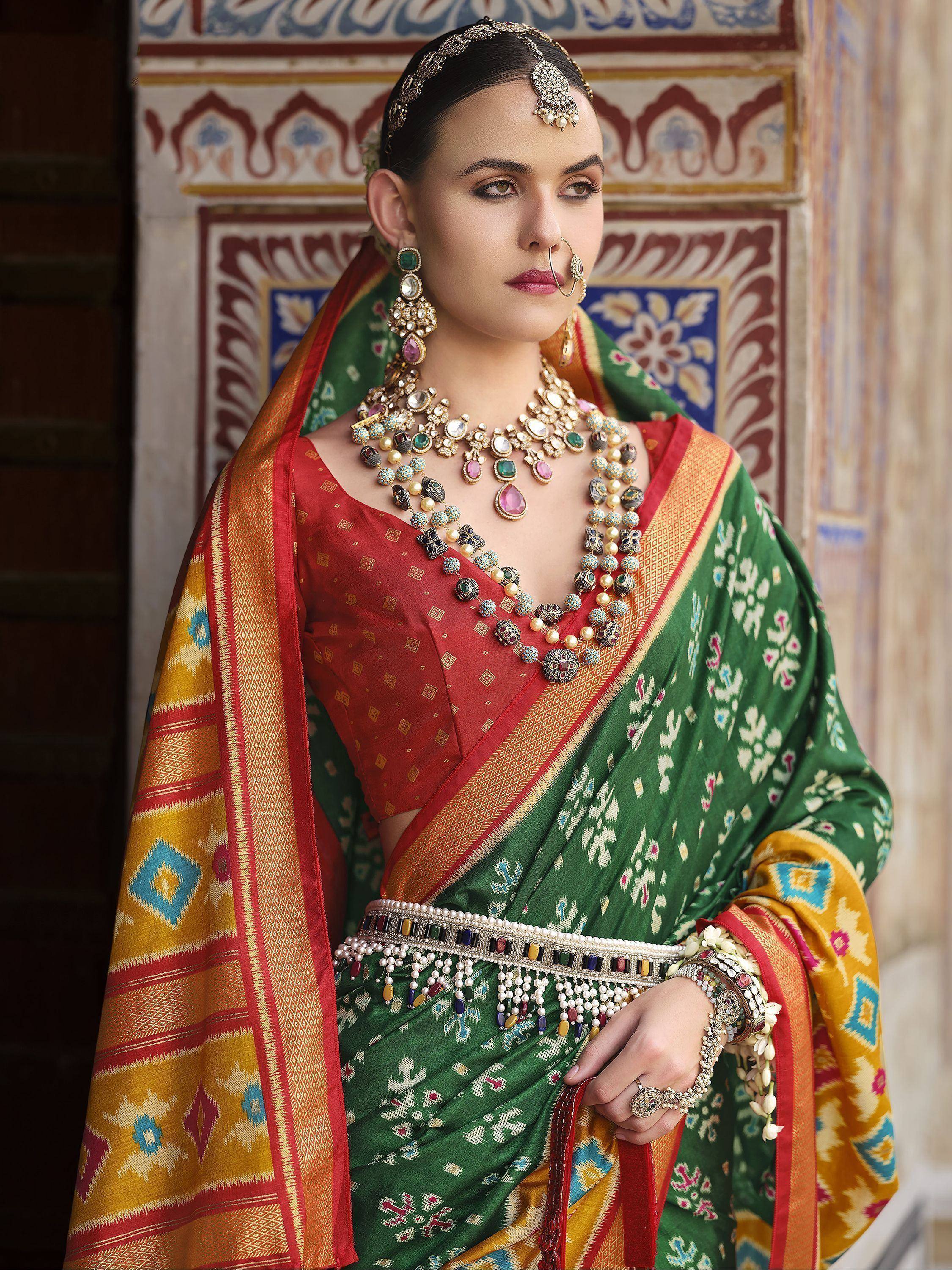 Woman in vibrant green and red Indian saree with traditional jewelry and temple backdrop