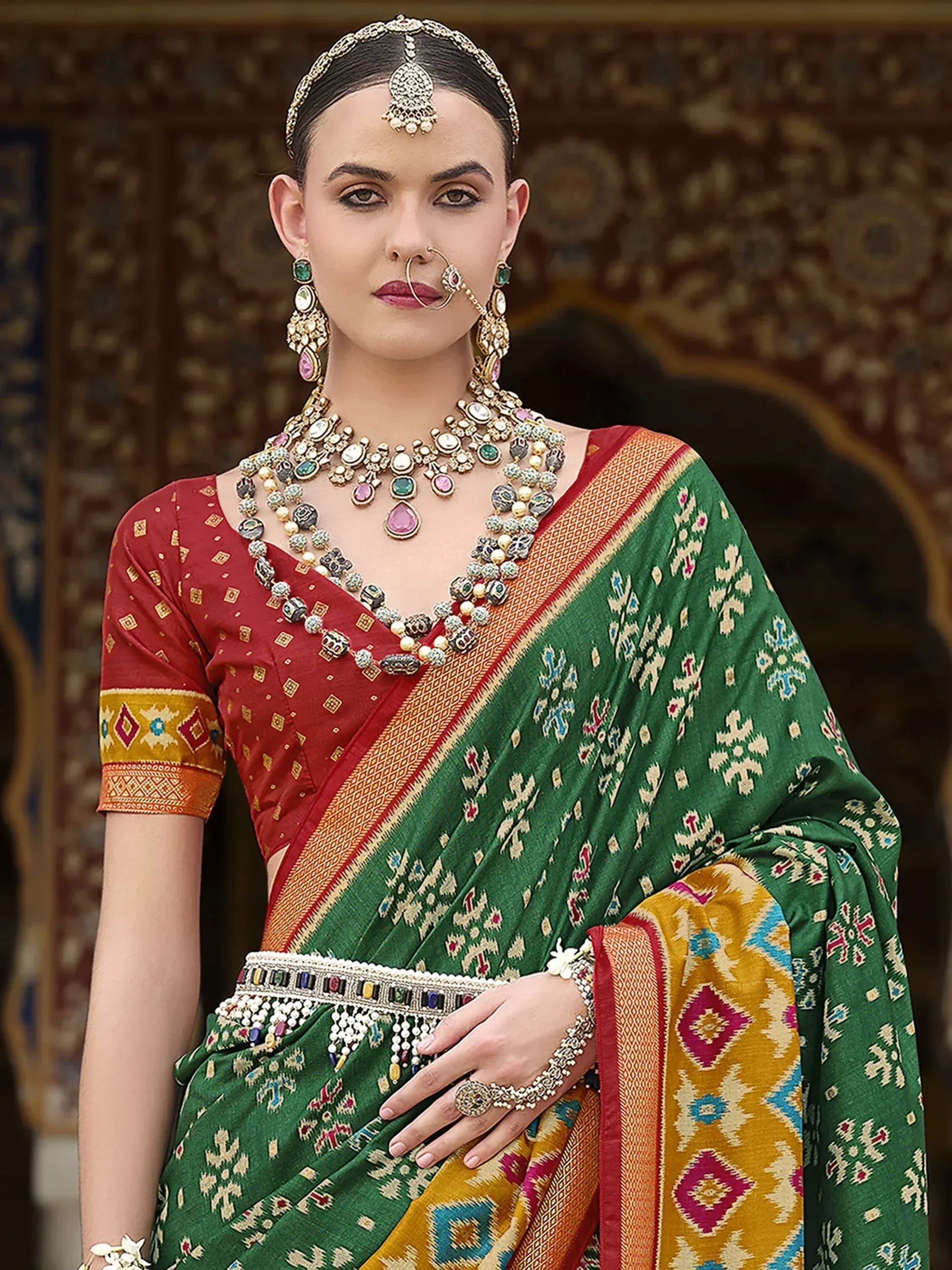 Green and red ethnic saree with intricate patterns, paired with traditional jewelry and maang tikka for Indian occasions