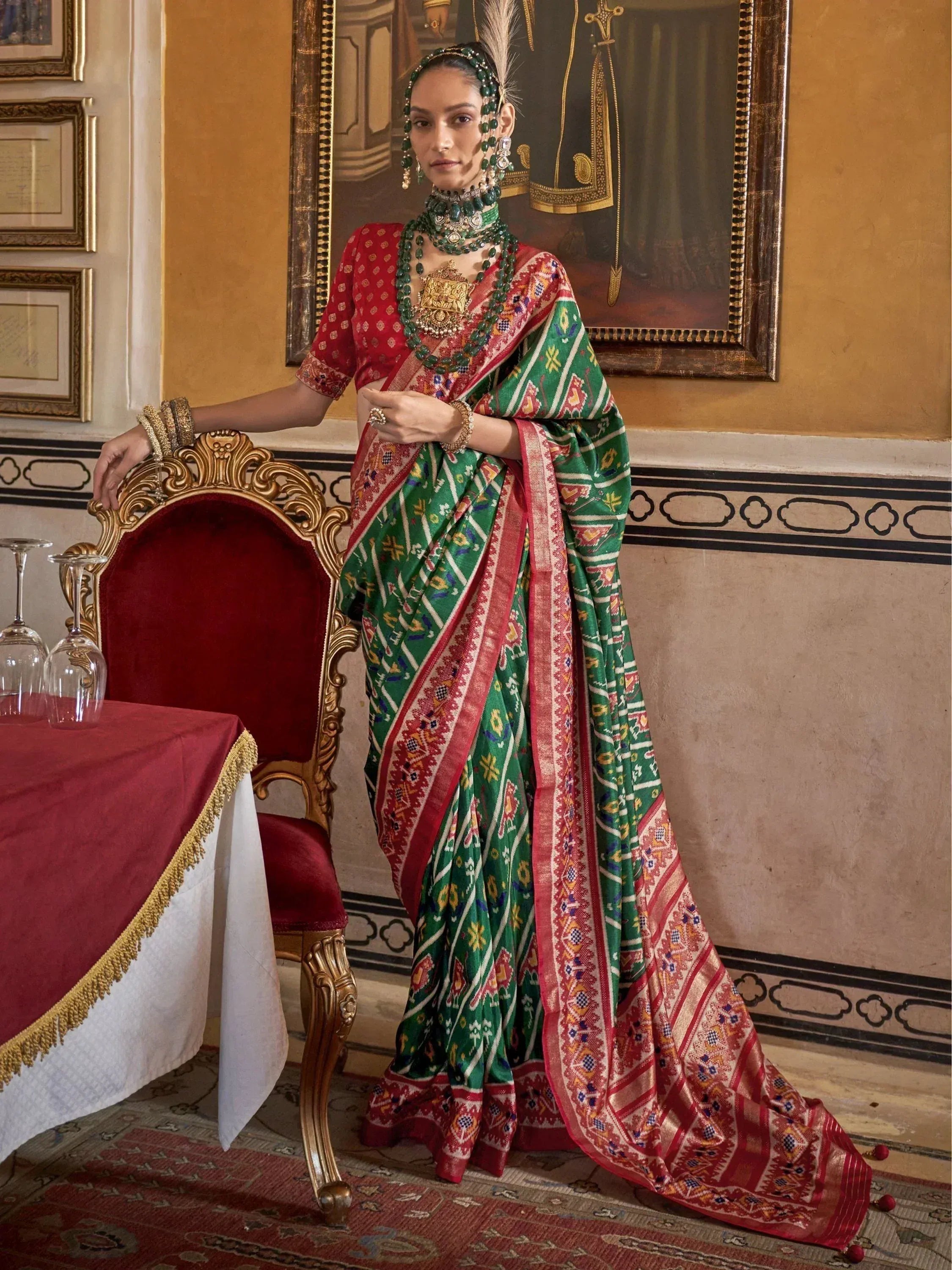 Woman in vibrant green and red ethnic saree with intricate patterns, traditional jewelry, and ornate setting