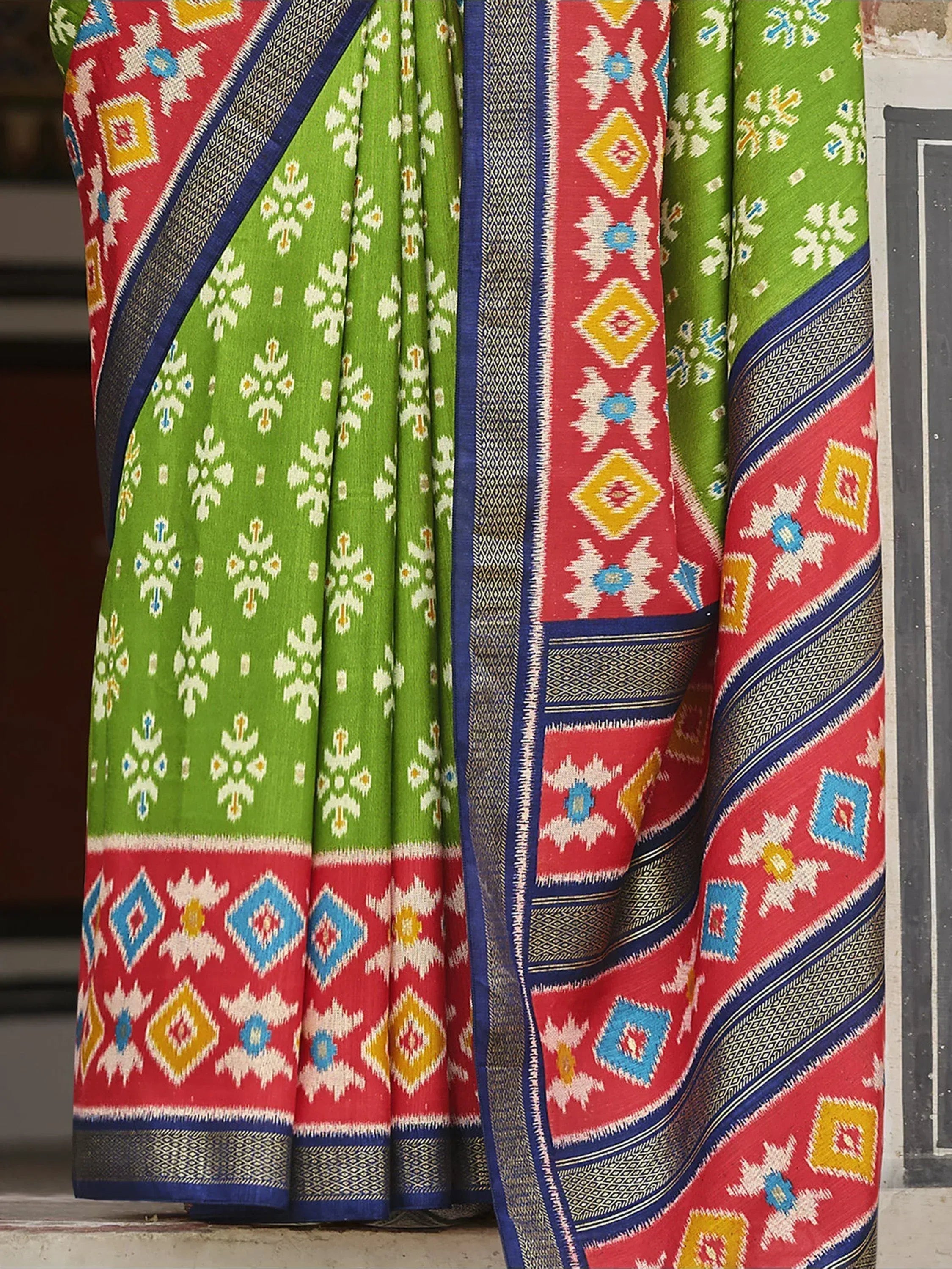 Vibrant green and red ethnic saree with geometric ikat patterns and blue border, perfect for Indian occasions.
