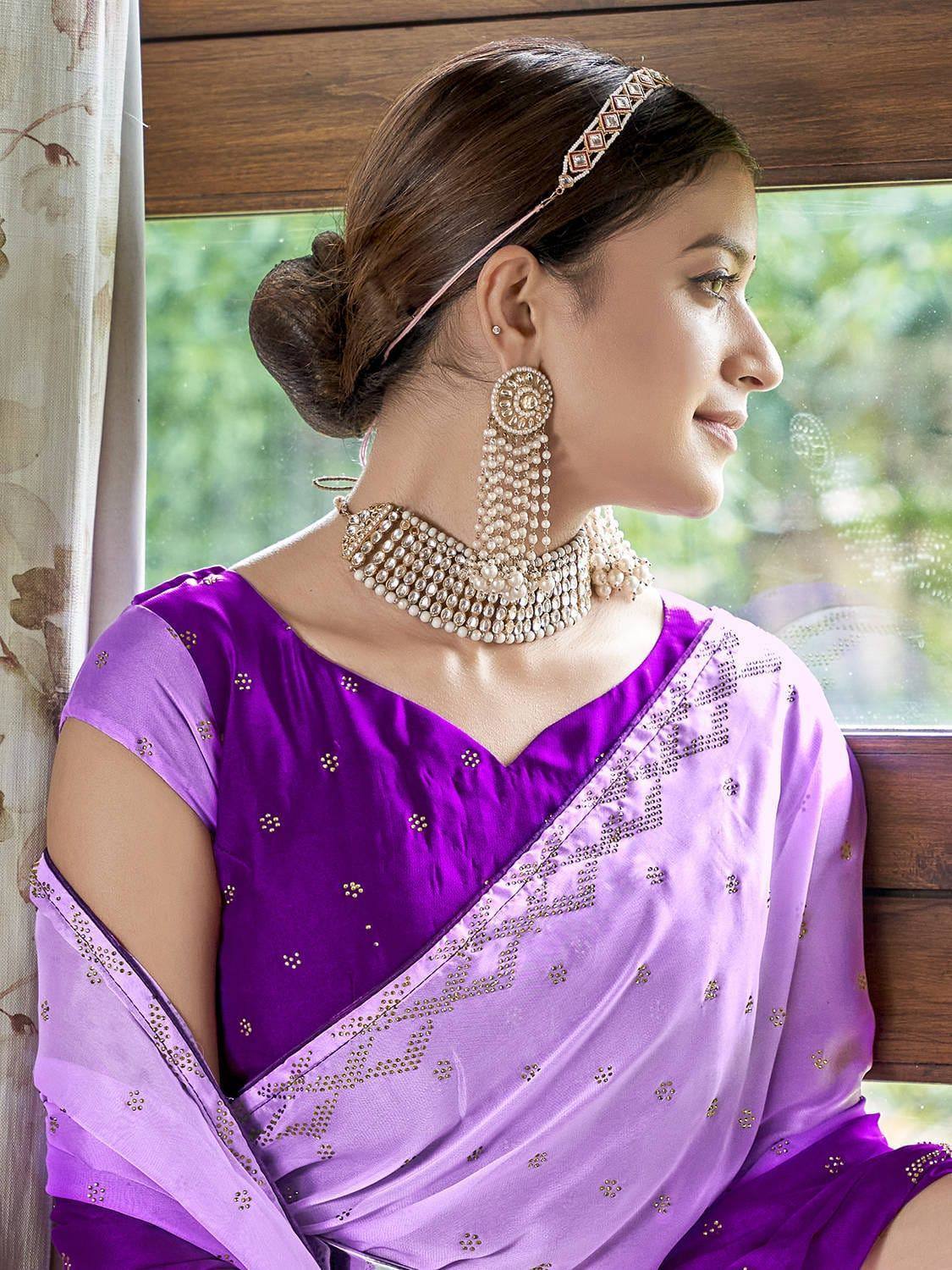 Woman in purple designer saree with gold embroidery, pearl jewelry, and traditional headpiece