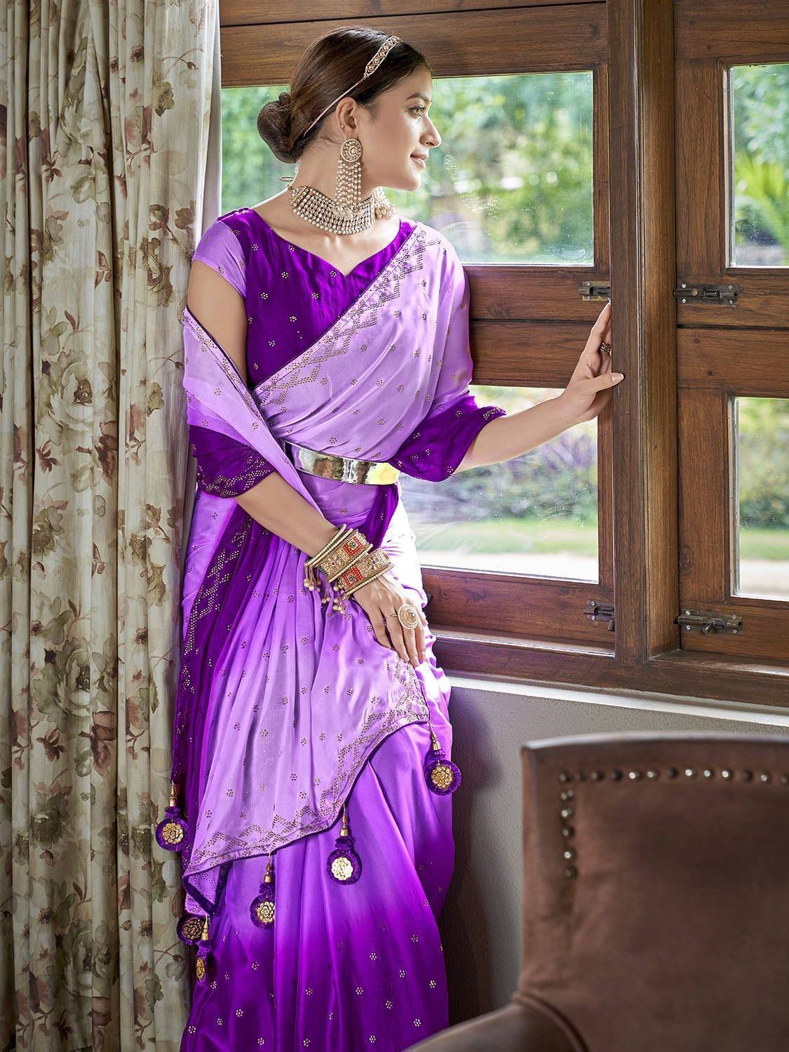 Woman in purple designer saree with gold embroidery, traditional Indian ethnic wear, standing by window