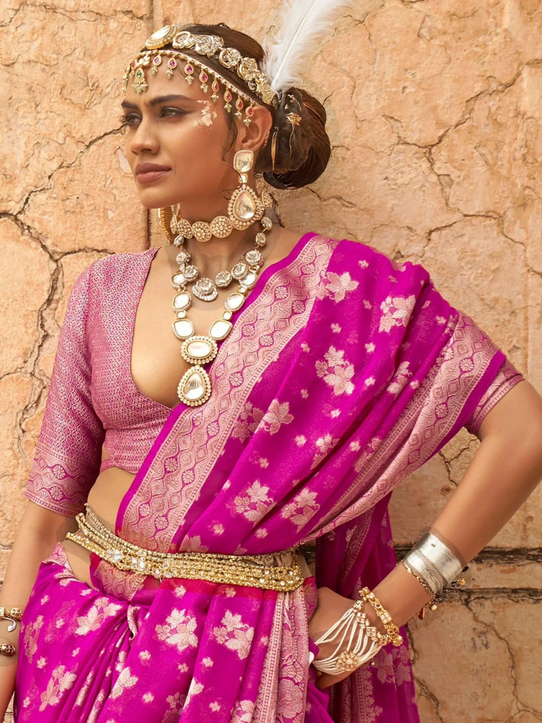 Woman in vibrant pink designer lehenga choli with gold jewelry and feather headpiece, ethnic Indian wear