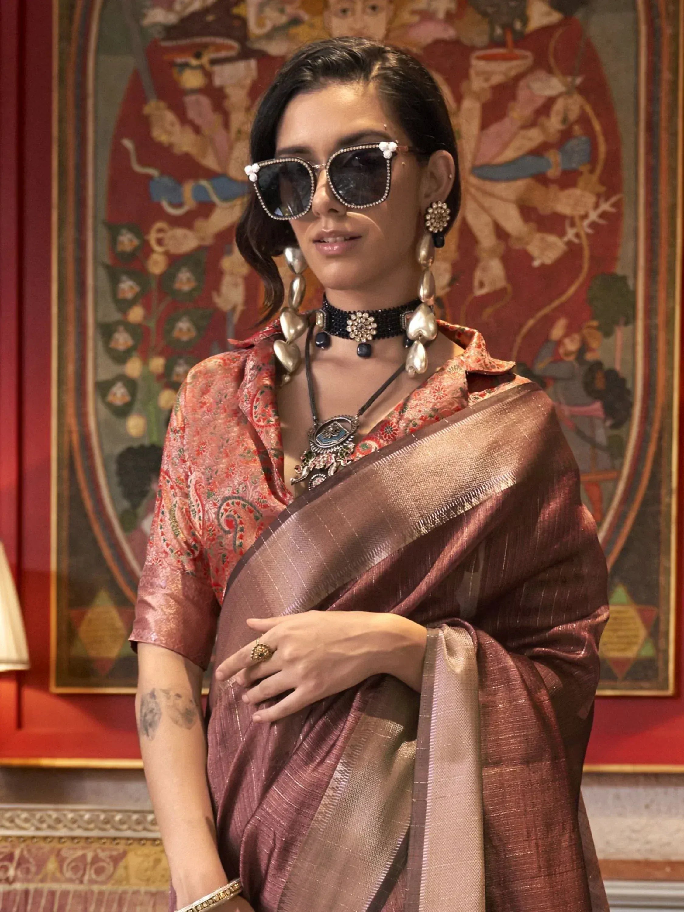 Woman in elegant ethnic saree with floral blouse, statement jewelry, and stylish sunglasses for festive occasions