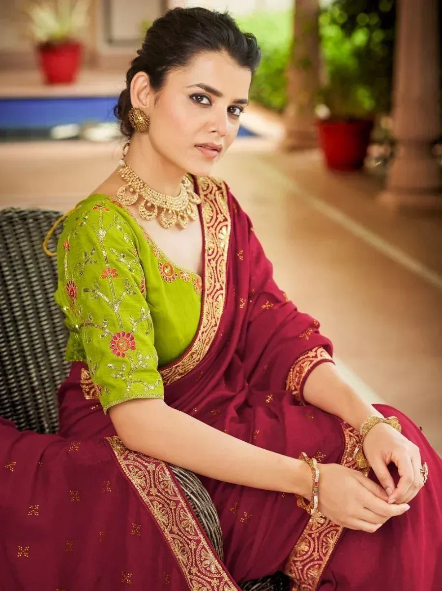 Woman in maroon saree with green embroidered blouse, gold jewelry, traditional Indian ethnic wear