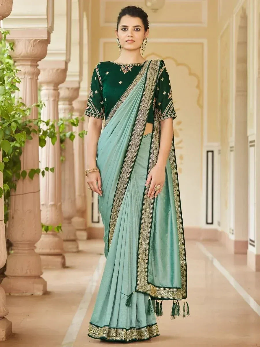Elegant light blue saree with green embroidered blouse, gold border, and tassels, perfect for Indian ethnic occasions.