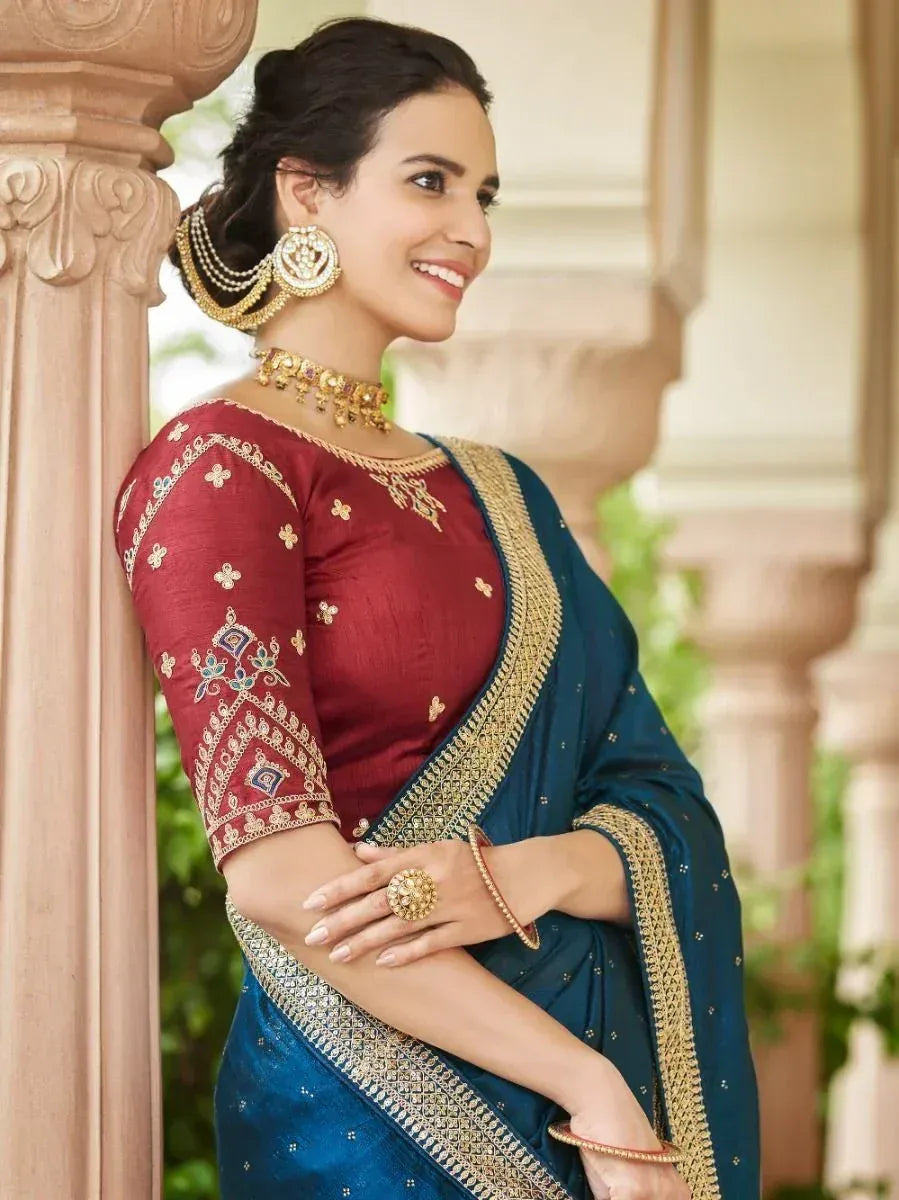 Woman in elegant blue saree with red blouse, gold embroidery, and traditional jewelry