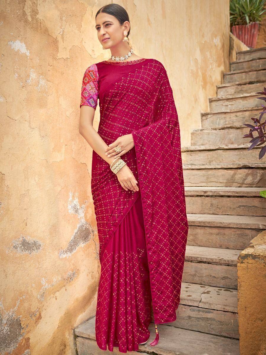 Woman in maroon embroidered saree with colorful blouse, standing on stone steps near rustic wall