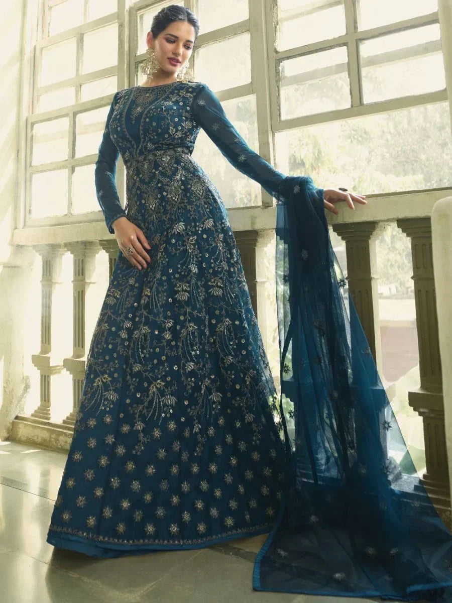 Woman in blue embroidered Indian ethnic gown with long sleeves and dupatta, standing indoors