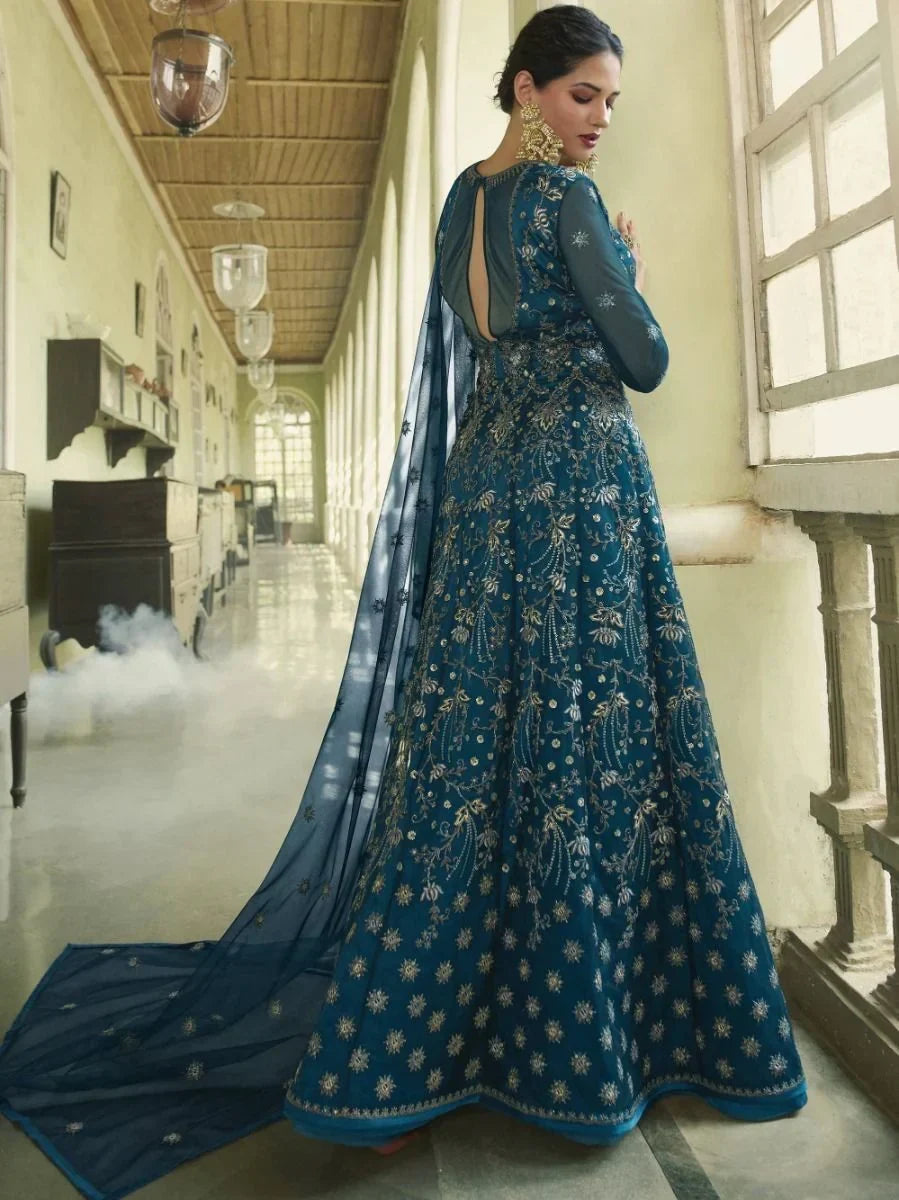 Woman in a blue embroidered ethnic gown with dupatta, standing in an elegant hallway