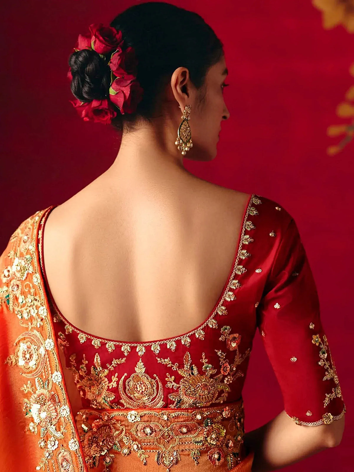 Red and gold embroidered lehenga choli with backless blouse, floral hair accessory, and jhumka earrings