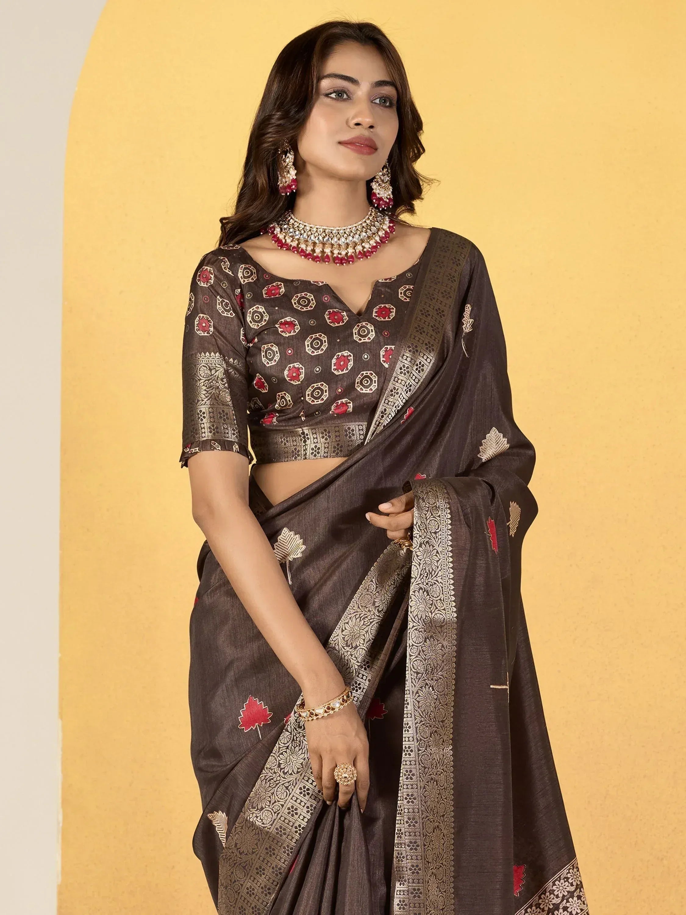 Brown ethnic saree with red floral print and gold border, paired with matching blouse and jewelry