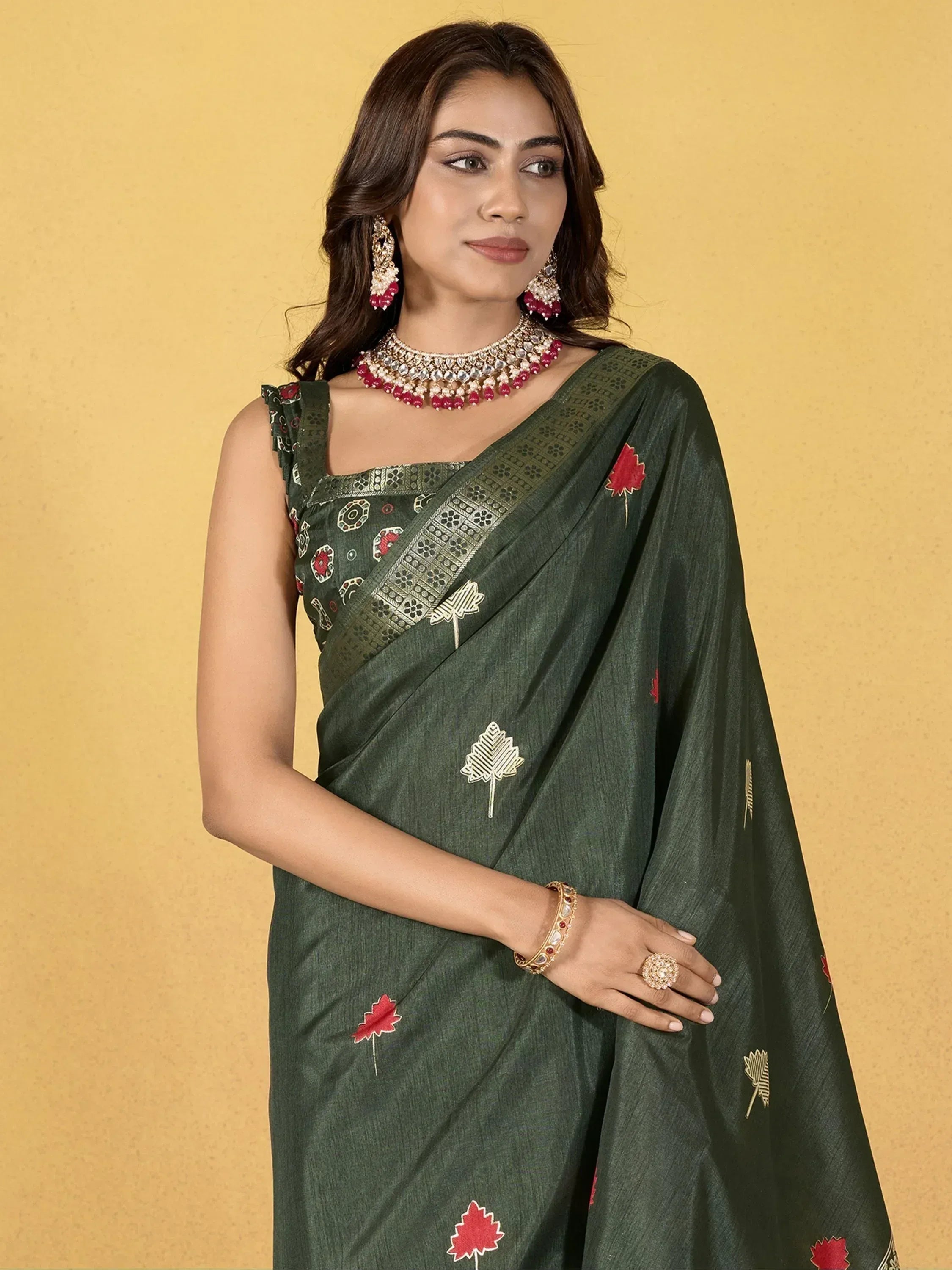 Woman in olive green embroidered saree with red and gold leaf motifs, paired with traditional jewelry.