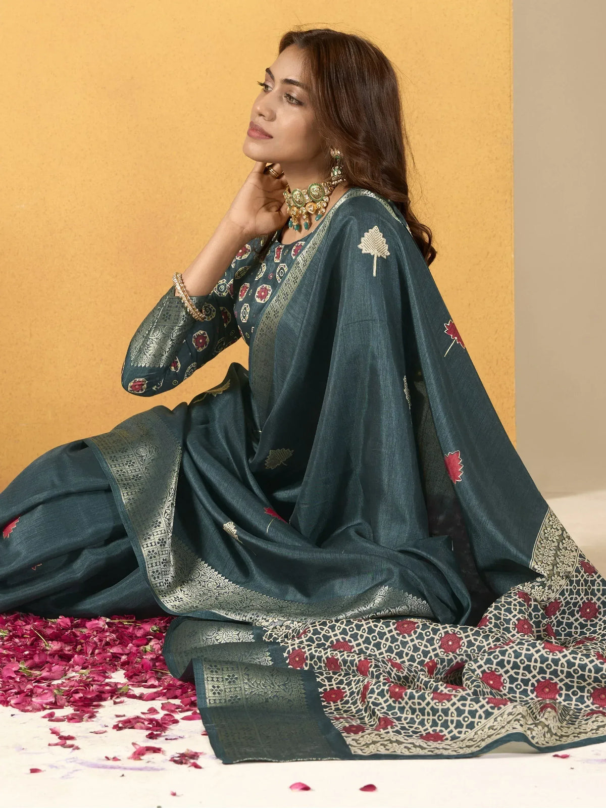 Woman in teal embroidered salwar kameez with floral motifs and gold border, styled with traditional jewelry.