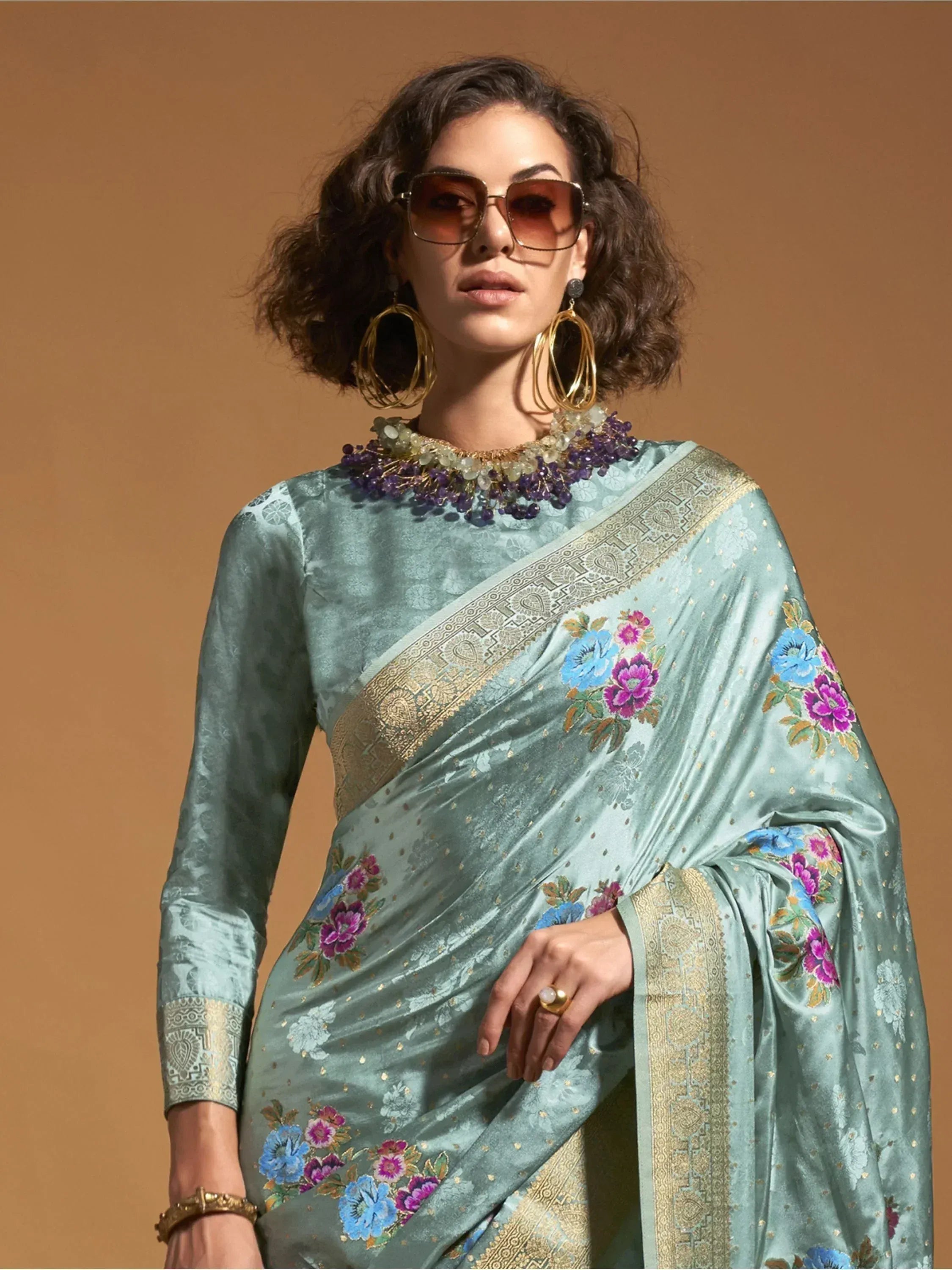 Woman in elegant mint green saree with floral embroidery and gold border, styled with statement jewelry.