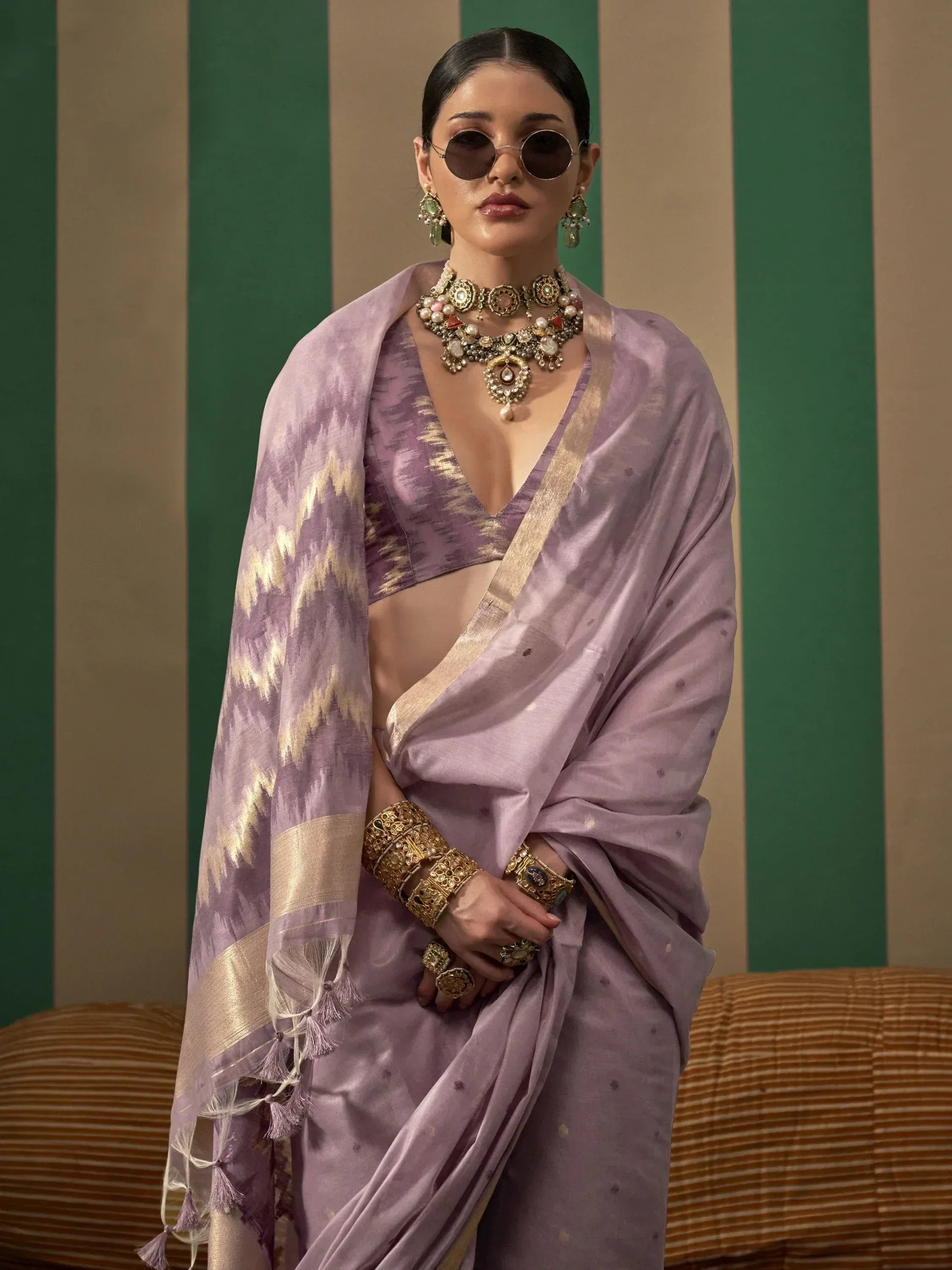 Lavender ikat saree with gold border, paired with statement jewelry and sunglasses for a modern ethnic look.