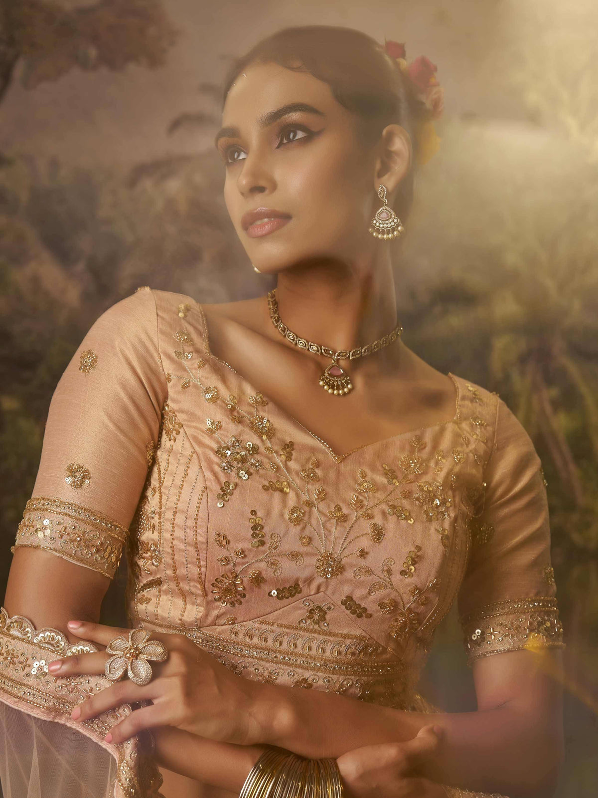 Elegant woman in peach designer lehenga choli with gold embroidery, floral hair accessories, and traditional jewelry