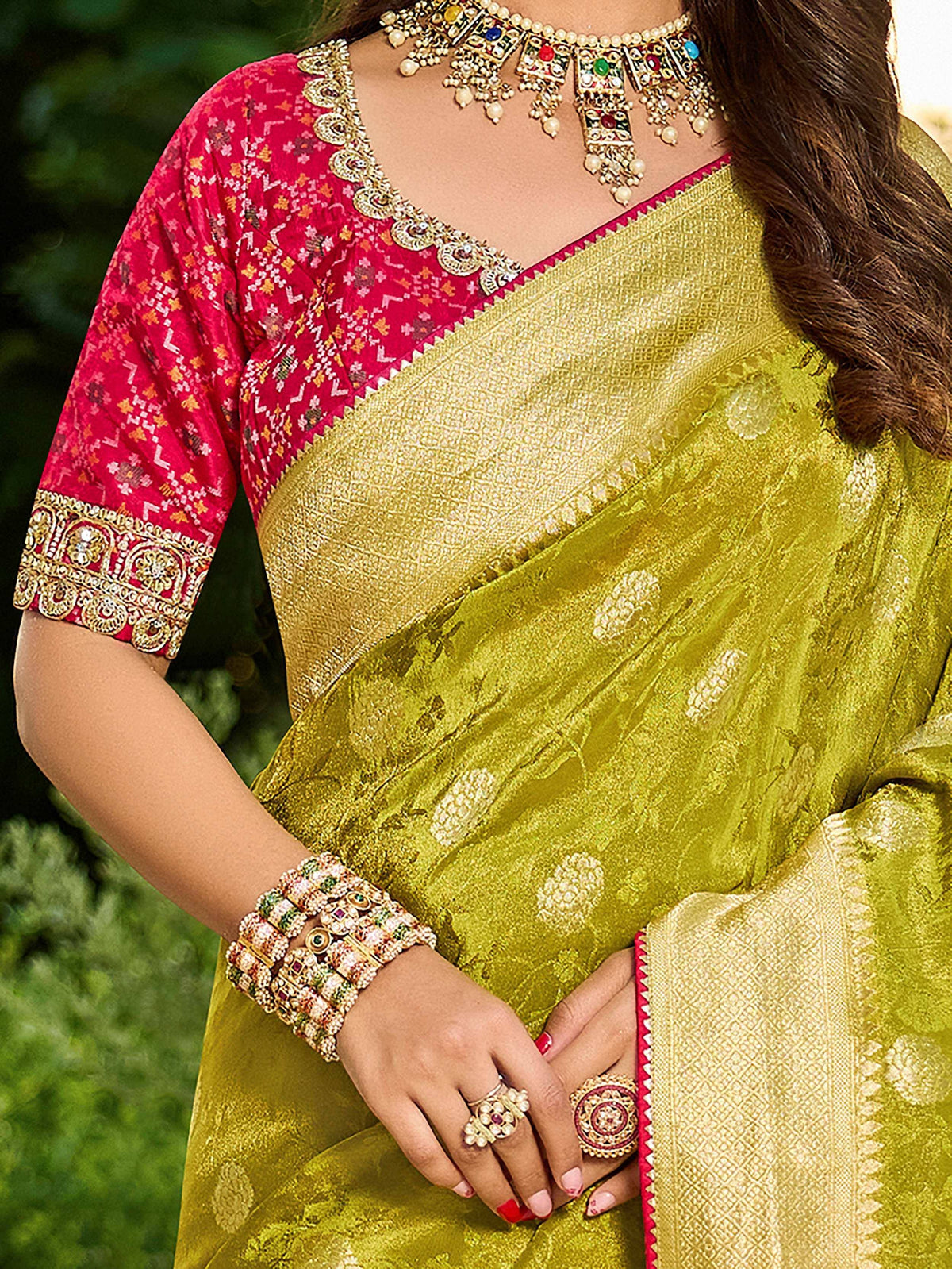 Woman in vibrant green saree with pink embroidered blouse, adorned with traditional Indian jewelry.