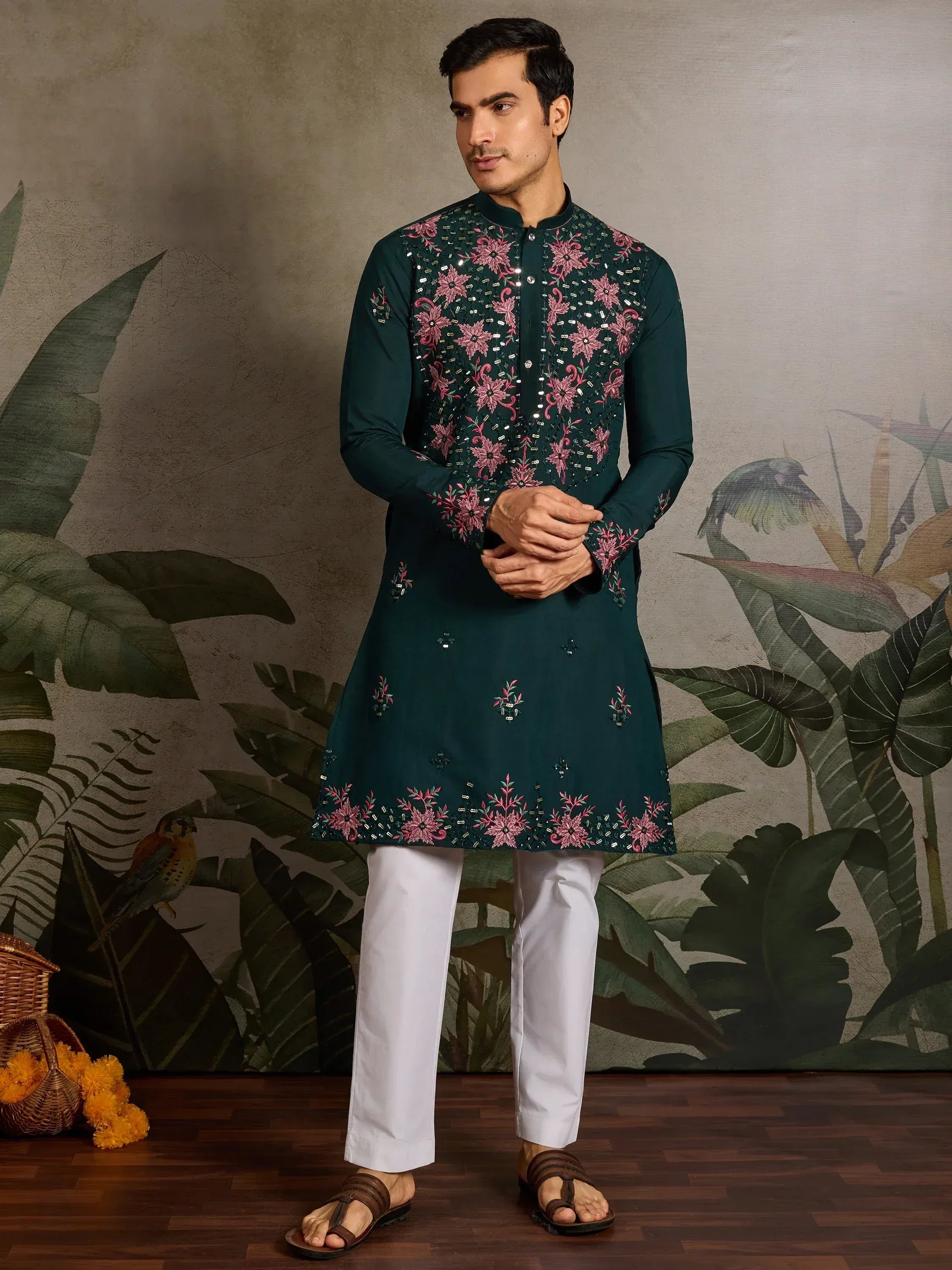 Man wearing dark green embroidered kurta with pink floral design, white pants, and sandals for ethnic occasions