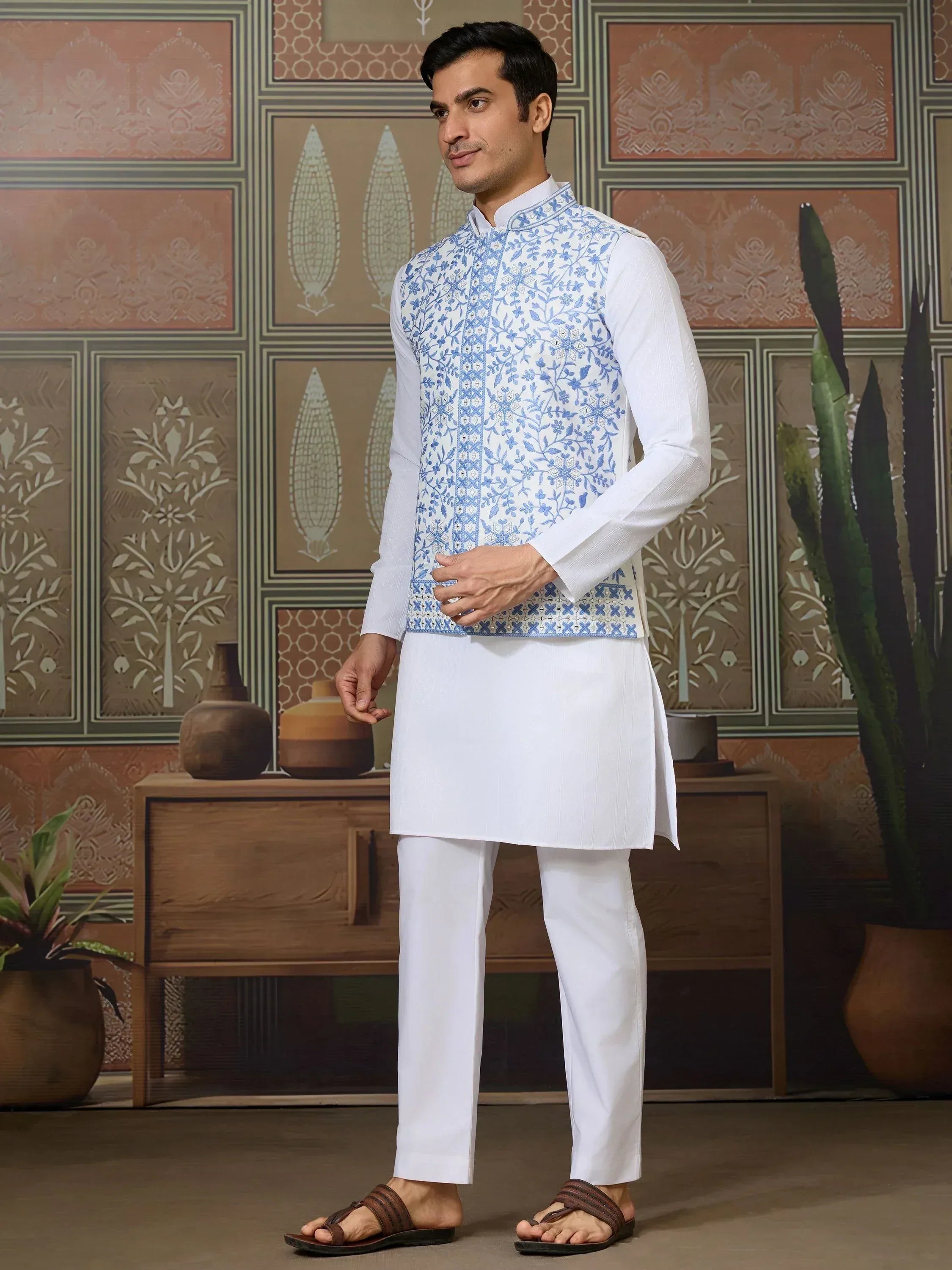 Man in white kurta pajama with blue floral embroidered vest, ethnic Indian wear