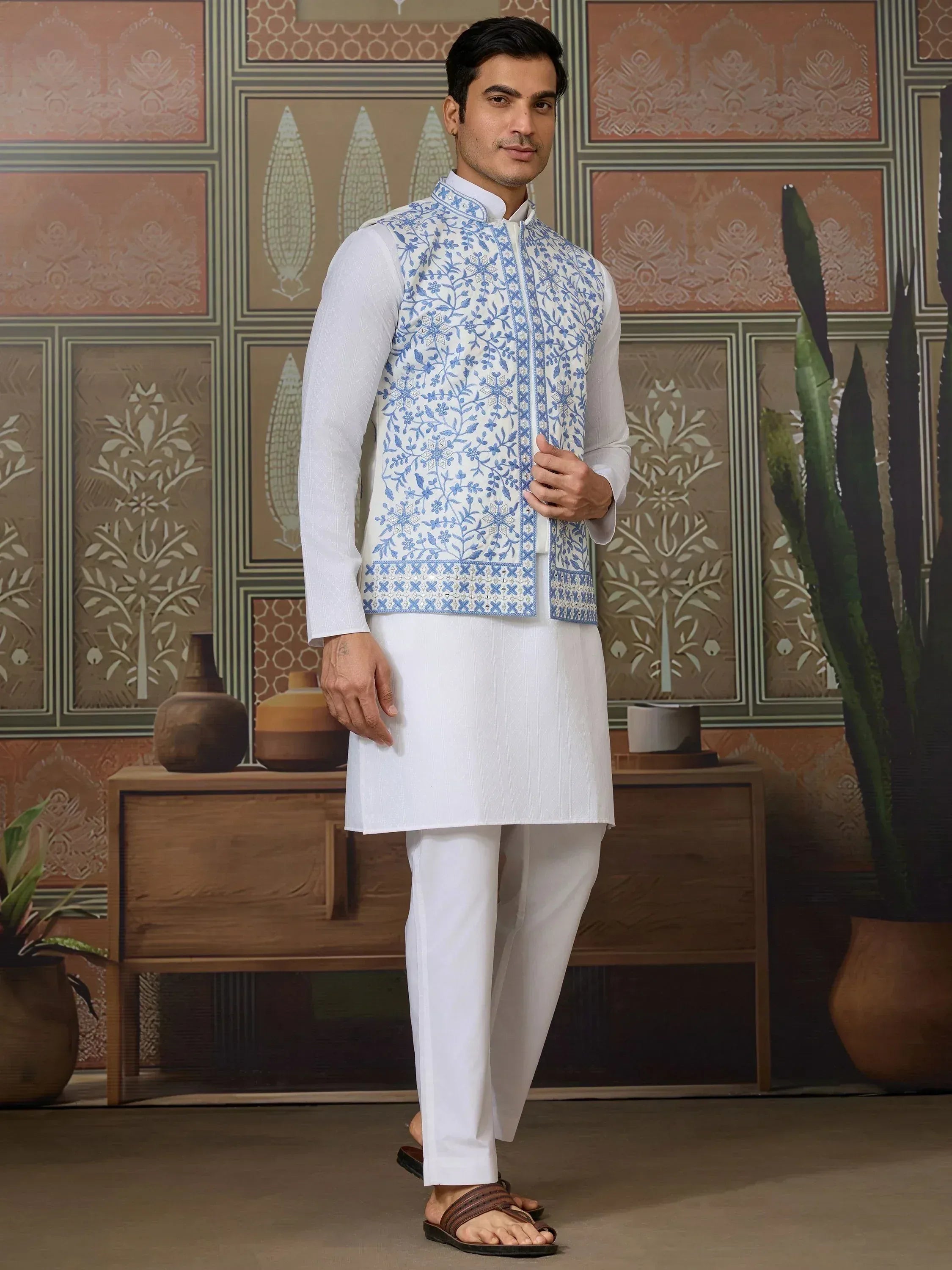 Man in white kurta pajama with blue floral embroidered vest, ethnic Indian wear