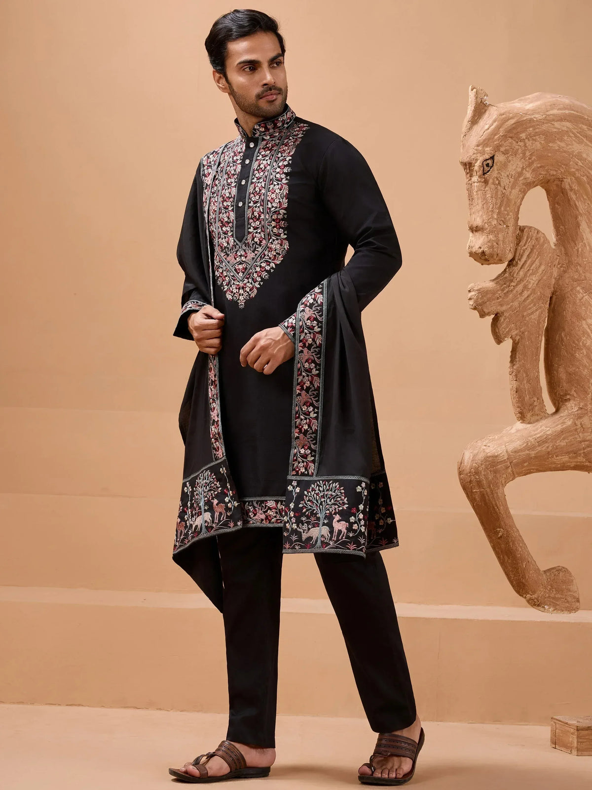 Man wearing black embroidered kurta with floral and deer motifs, paired with churidar pants for ethnic wear.