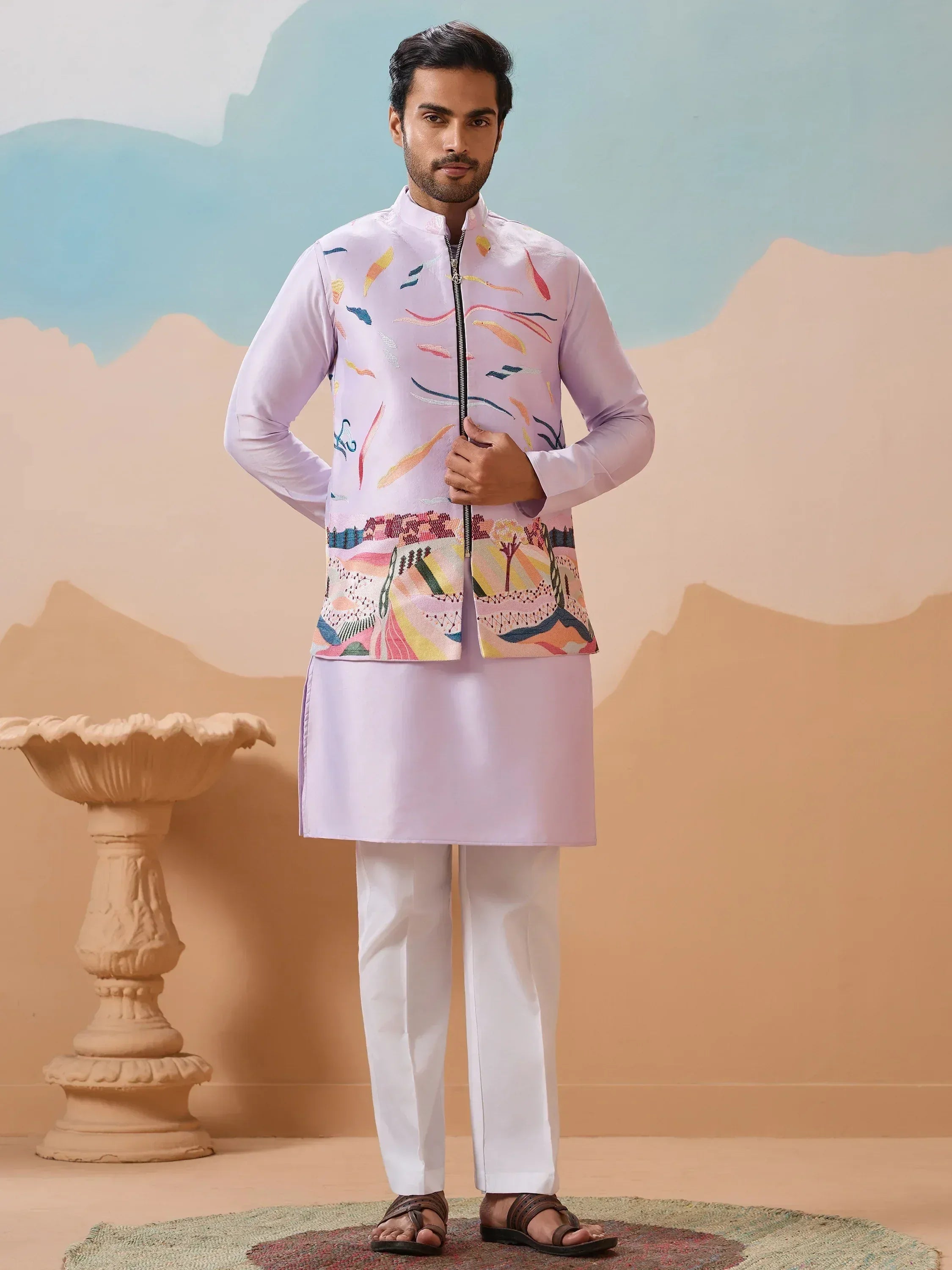 Man in lavender kurta with colorful embroidered jacket, white pants, ethnic Indian wear