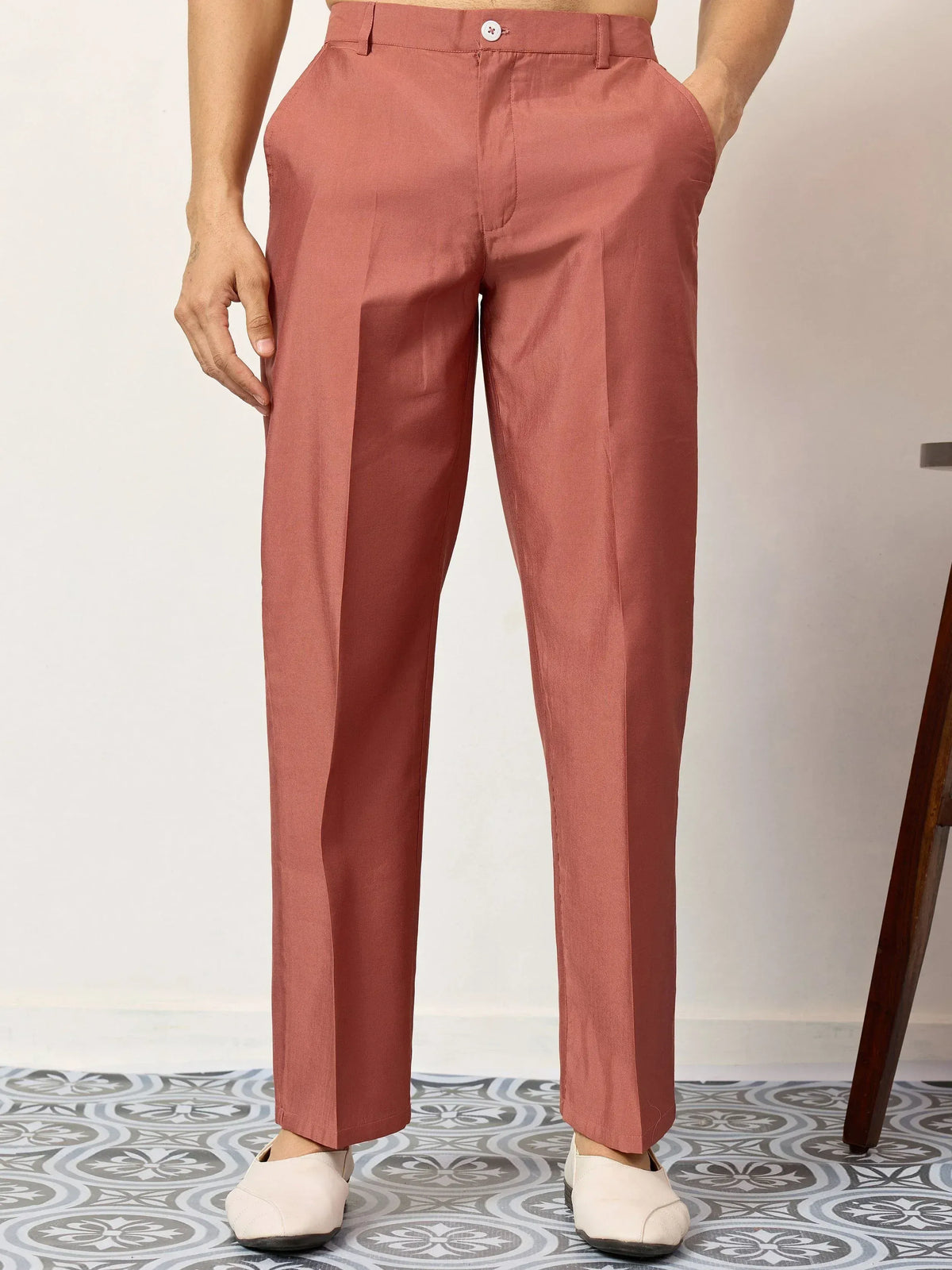Men's rust-colored formal trousers with sleek fit and white button detail, paired with beige loafers.