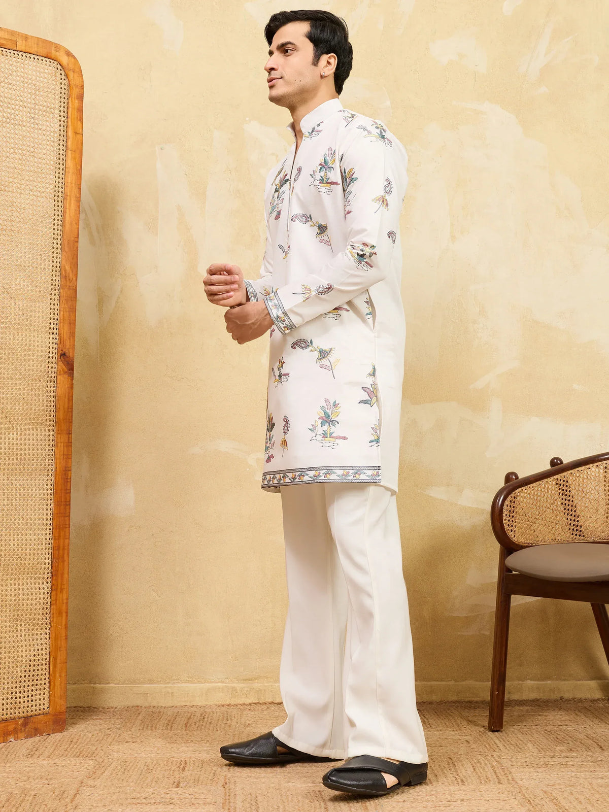 Man wearing a white floral printed kurta with matching trousers and black loafers.