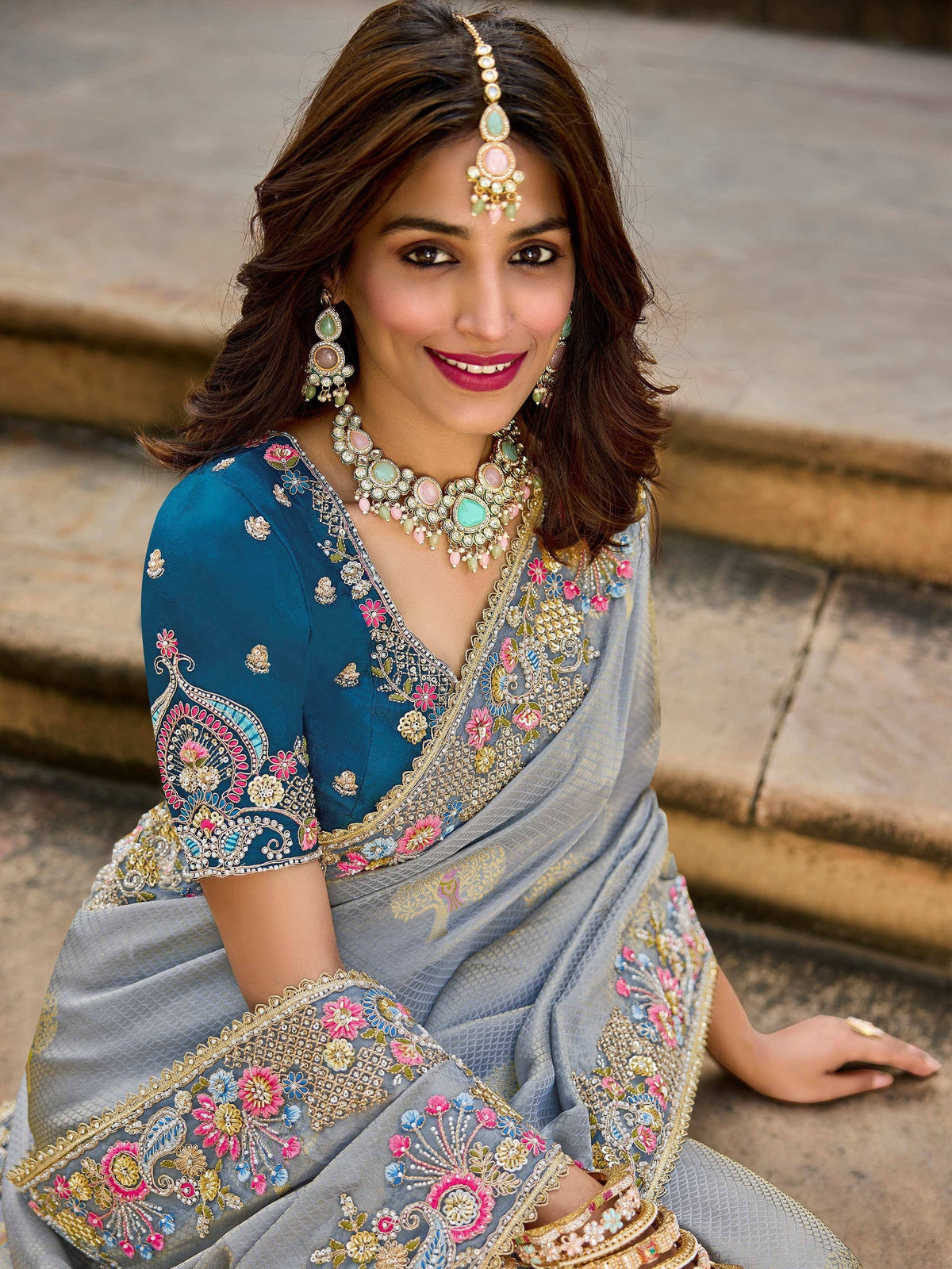 Woman in elegant grey saree with floral embroidery and blue blouse, paired with traditional Indian jewelry