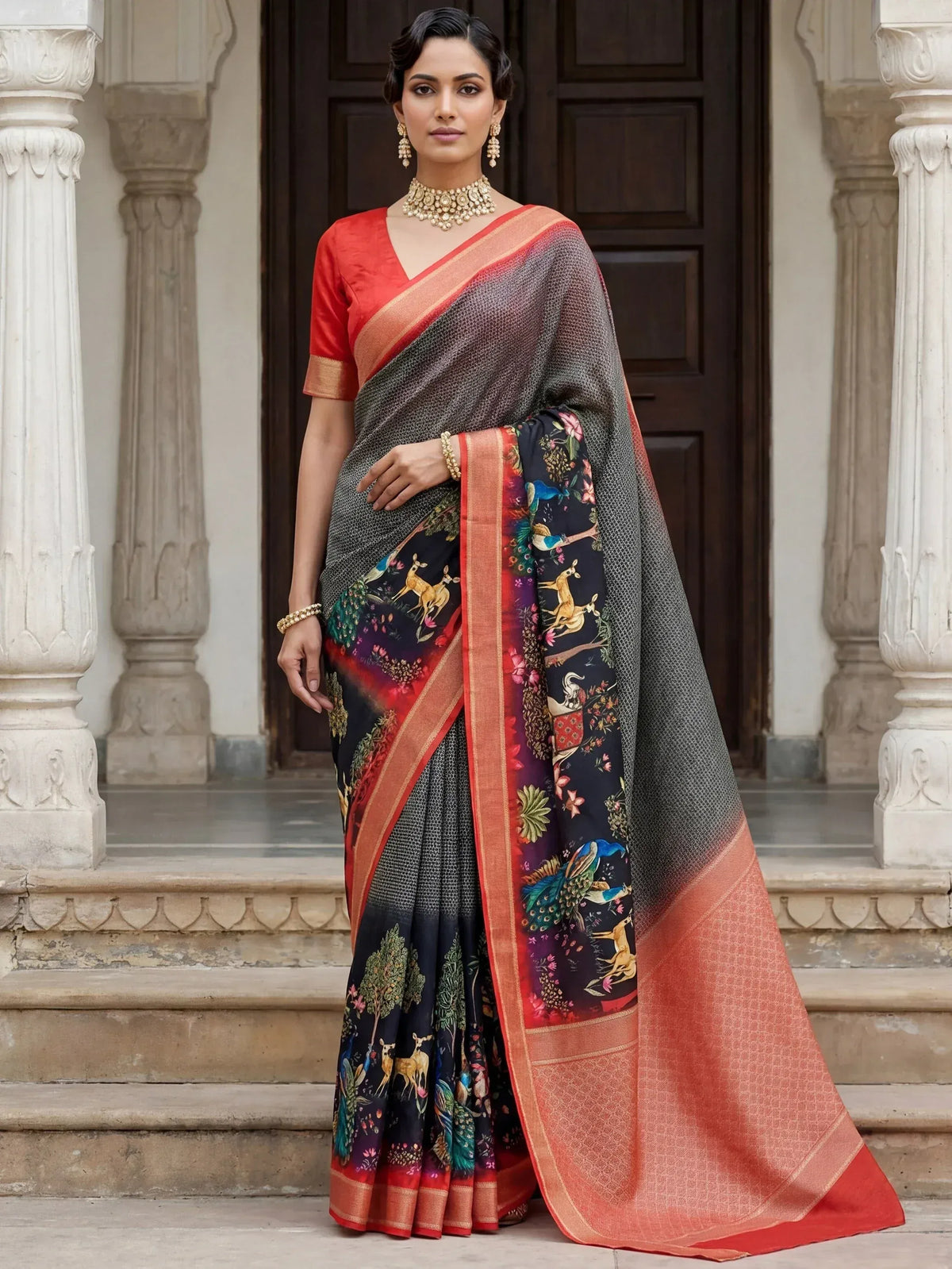 Woman in black and orange printed saree with peacock and deer motifs, paired with red blouse and gold jewelry