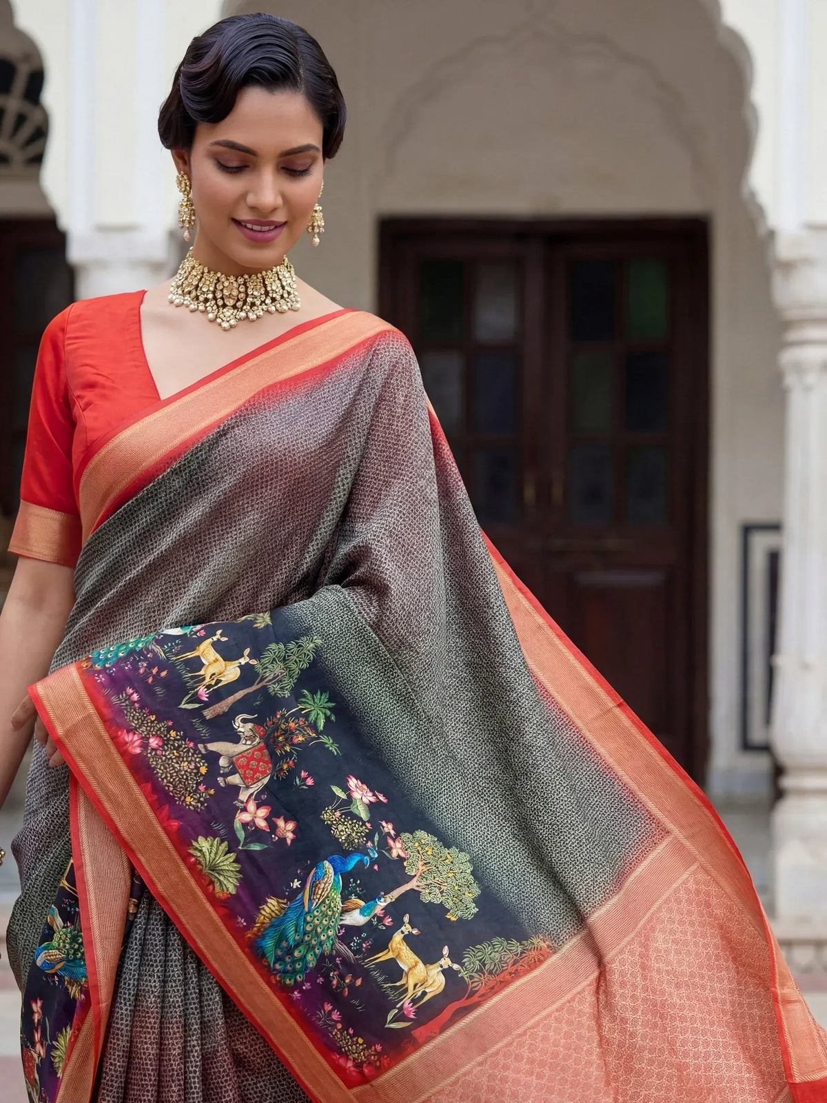 Woman in elegant Indian saree with peacock and deer print, orange border, paired with gold jewelry