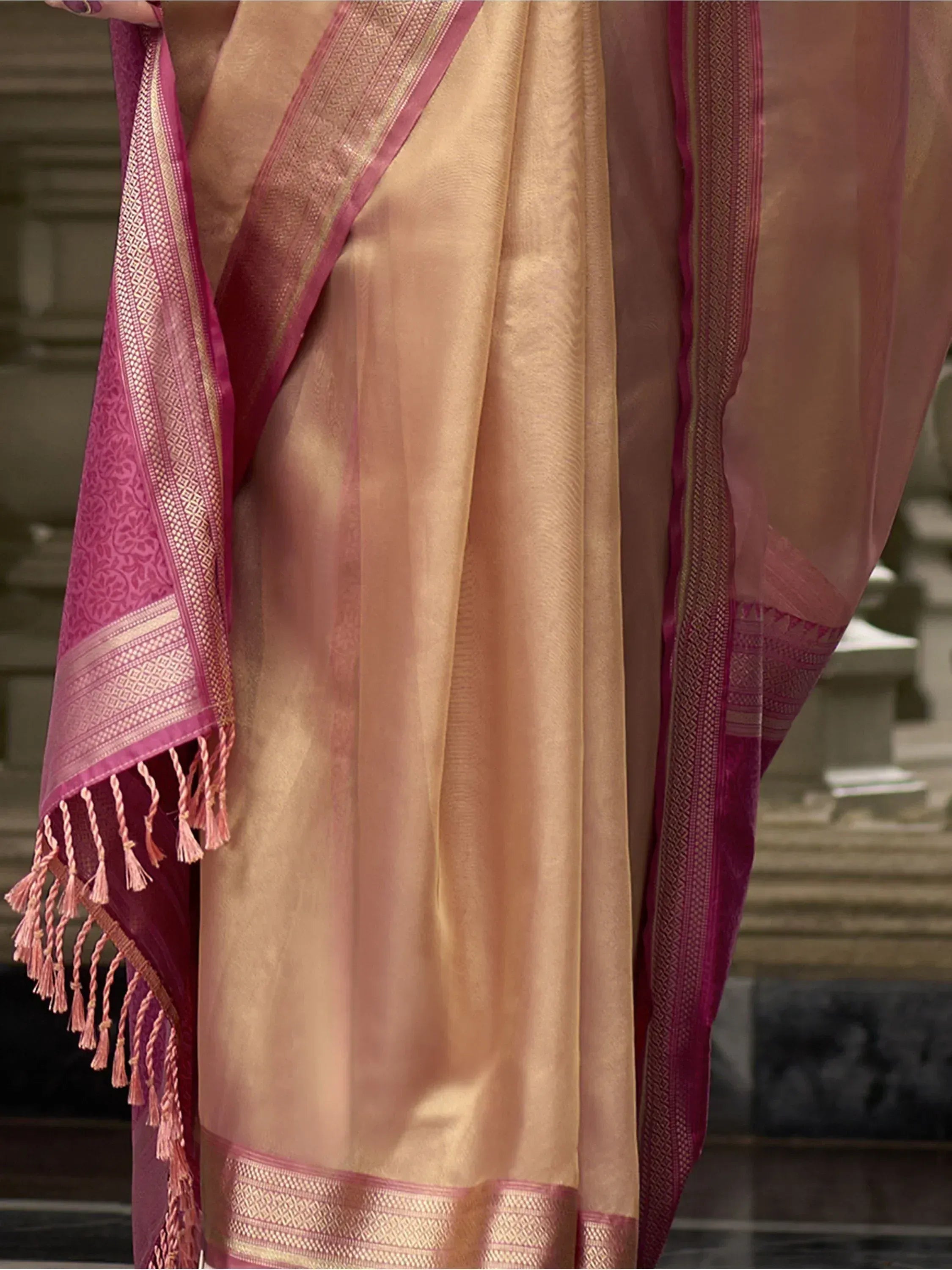 Elegant peach and pink ethnic saree with intricate gold border and tassels, perfect for Indian occasions
