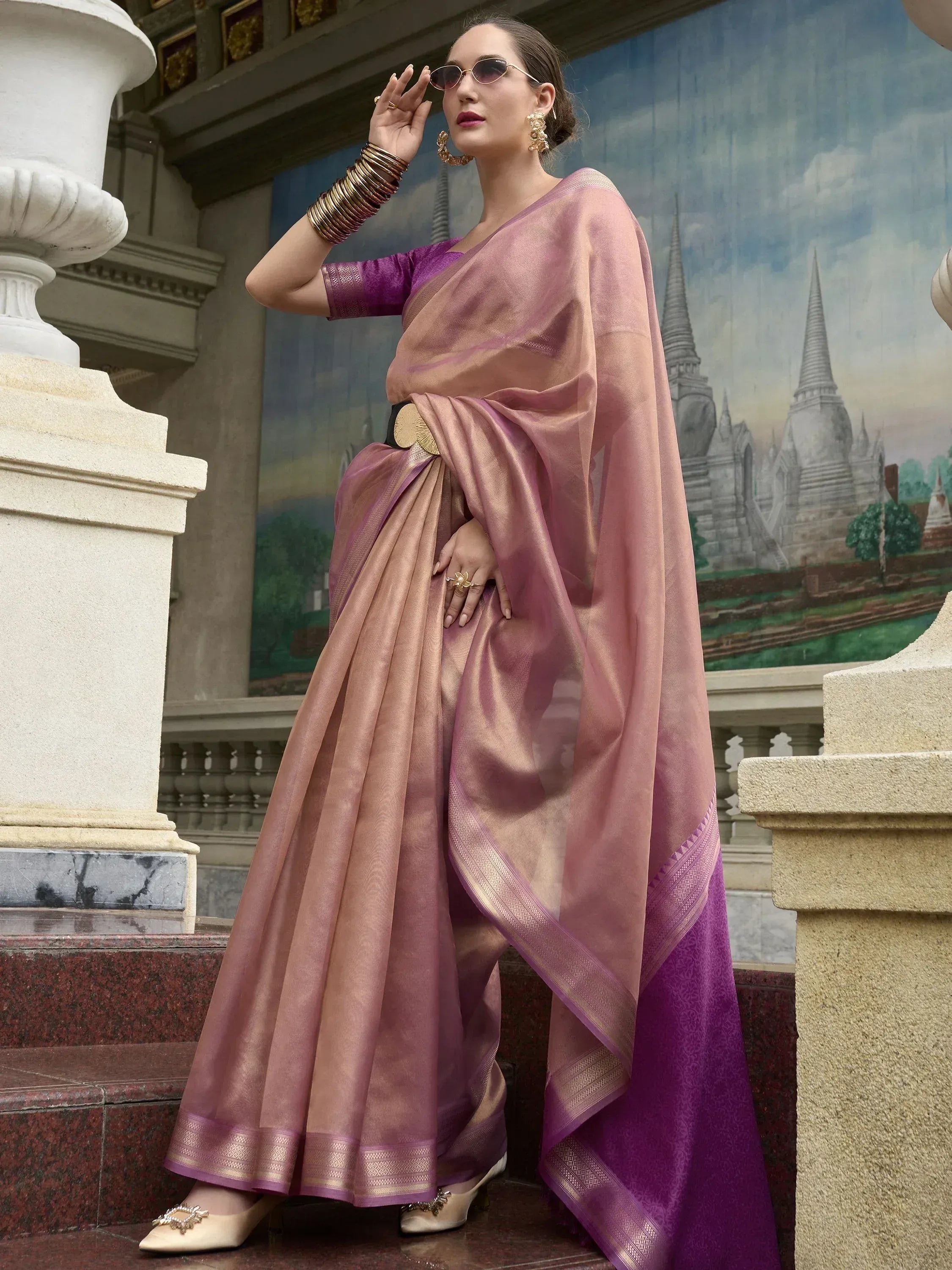 Elegant mauve and purple silk saree with gold border, styled with statement jewelry and sunglasses for festive occasions.