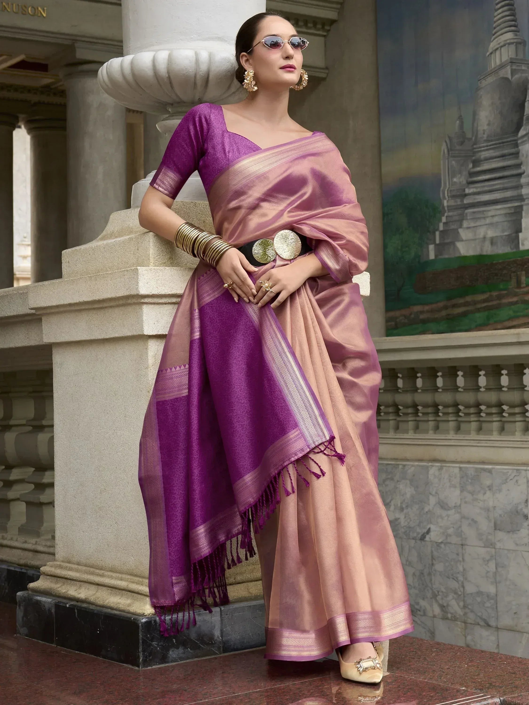 Woman in elegant purple and pink saree with gold border, styled with statement jewelry and sunglasses