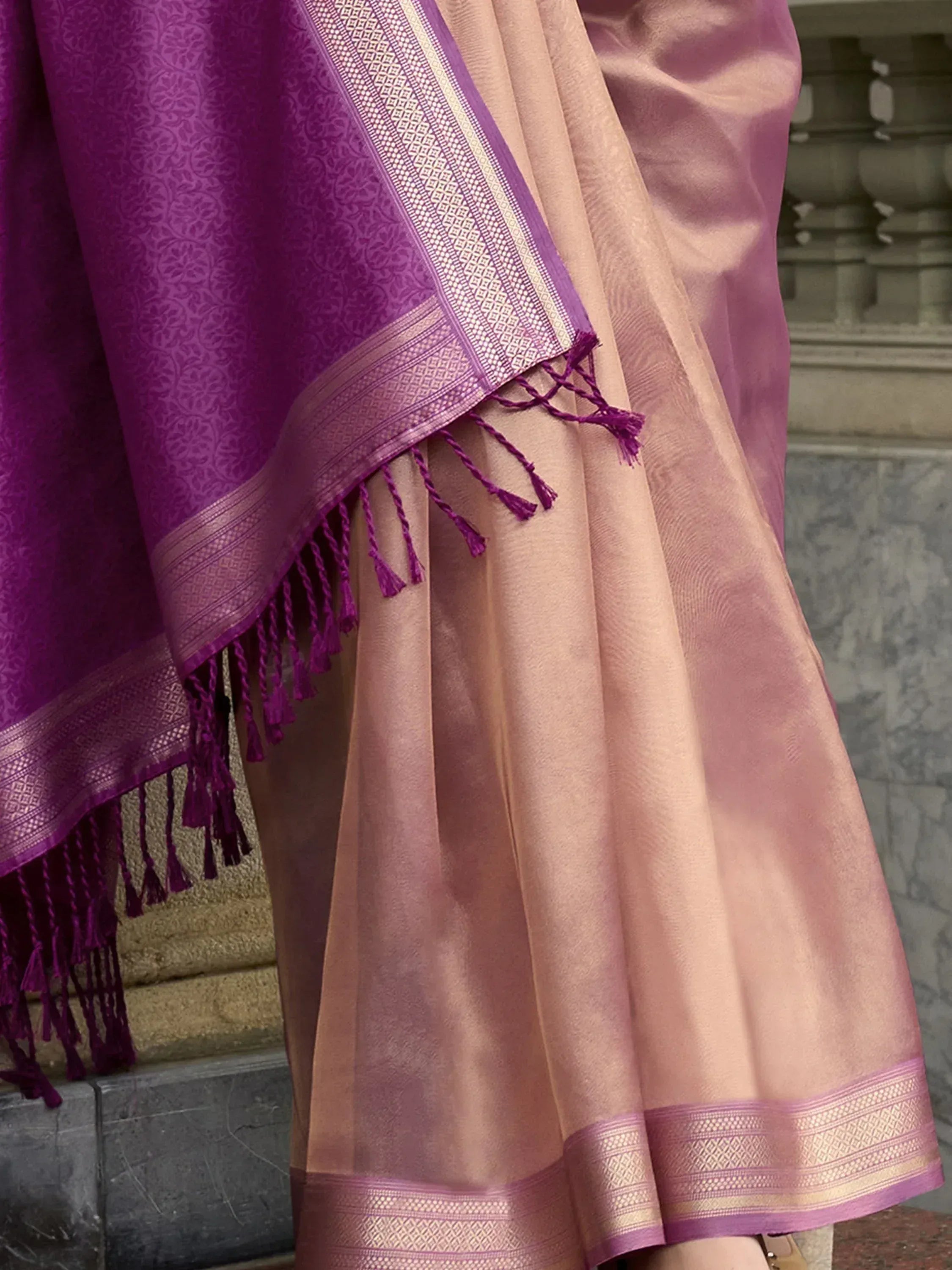 Elegant pink saree with purple border and tassels, featuring intricate woven patterns and traditional Indian design.