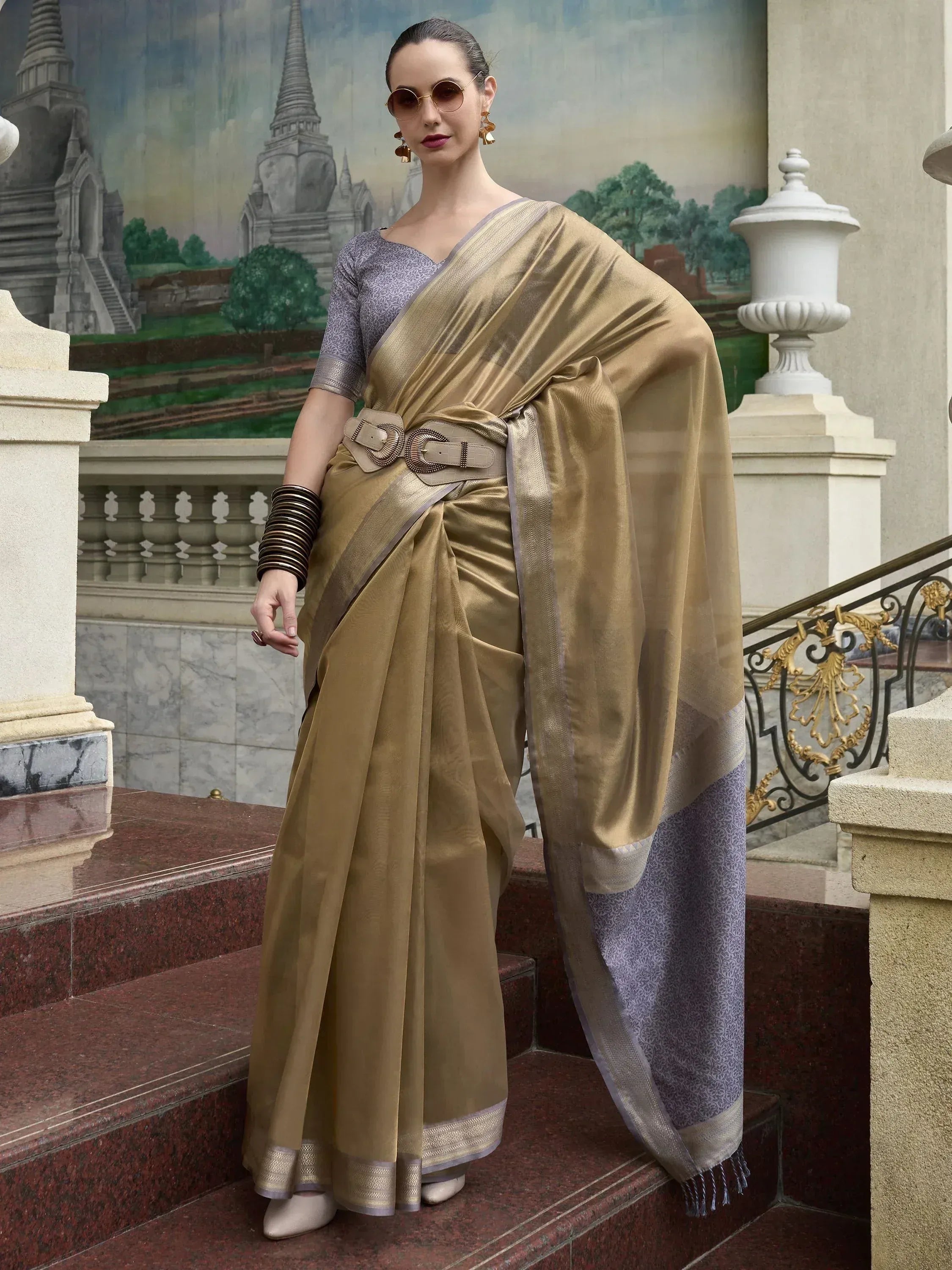 Elegant gold saree with purple blouse, designer belt, and temple backdrop for Indian ethnic wear