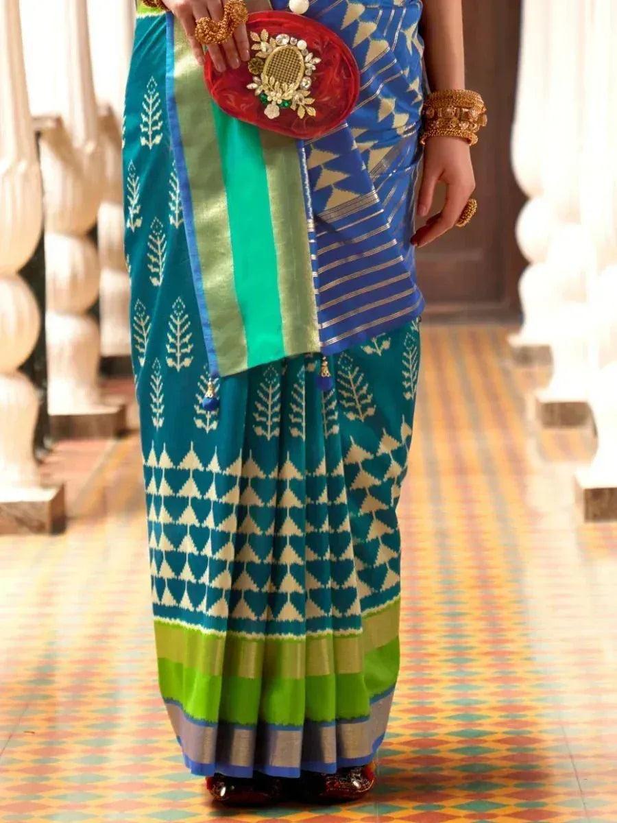 Teal and blue ikat saree with geometric patterns, paired with gold jewelry and red clutch