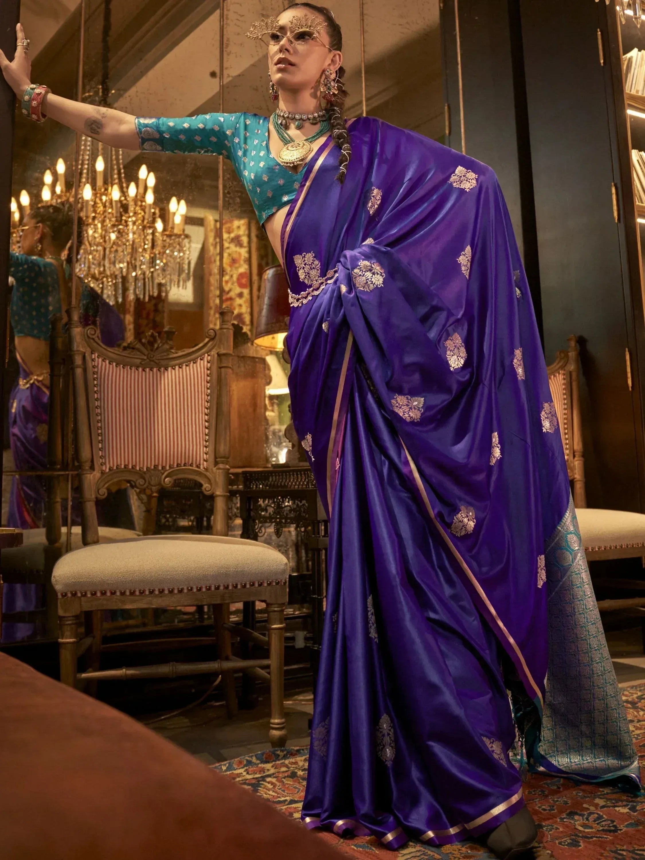 Woman in purple silk saree with gold embroidery and teal blouse, styled with traditional jewelry for ethnic wear.