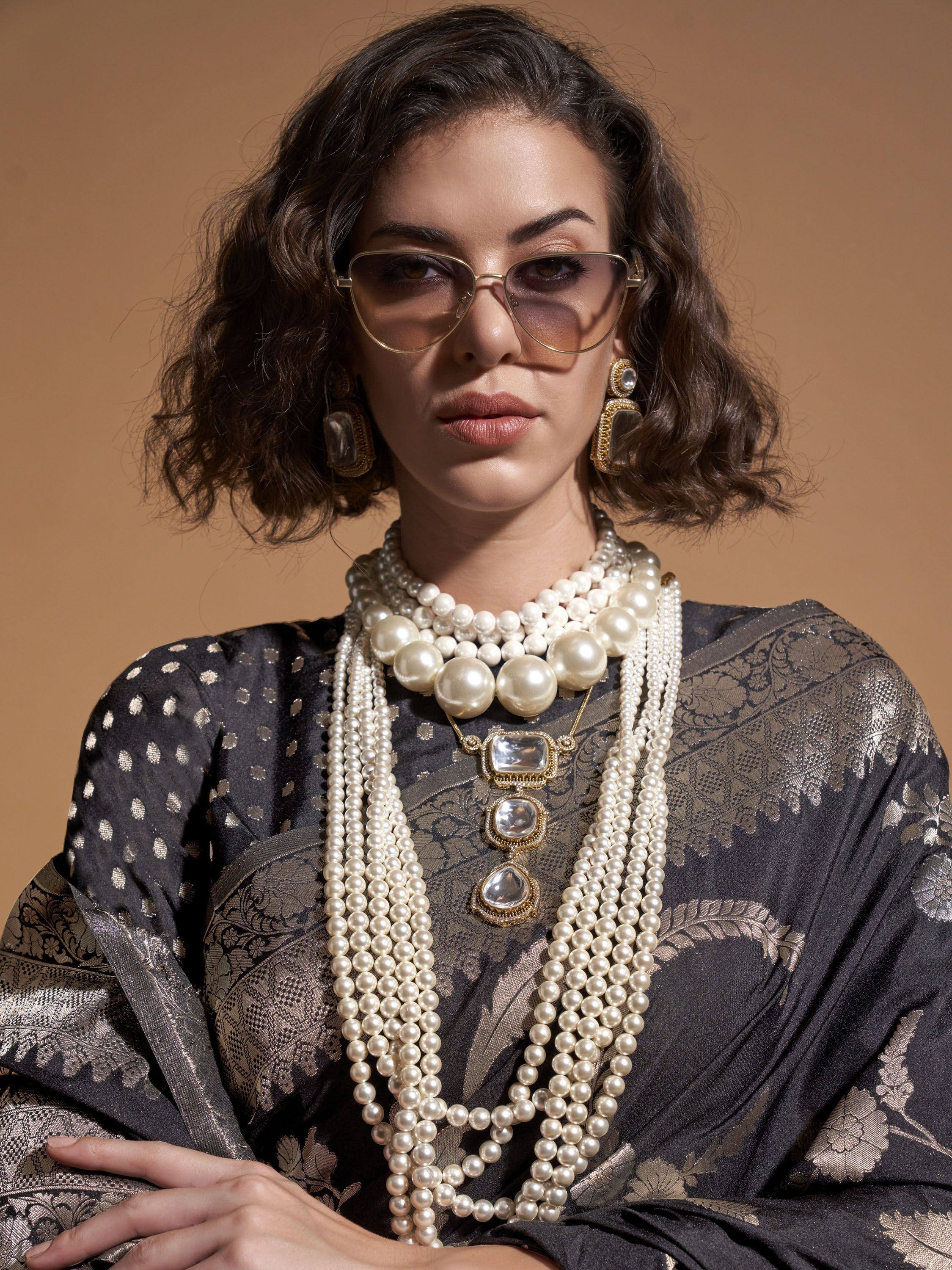 Woman in black and gold ethnic saree with layered pearl necklace and statement earrings