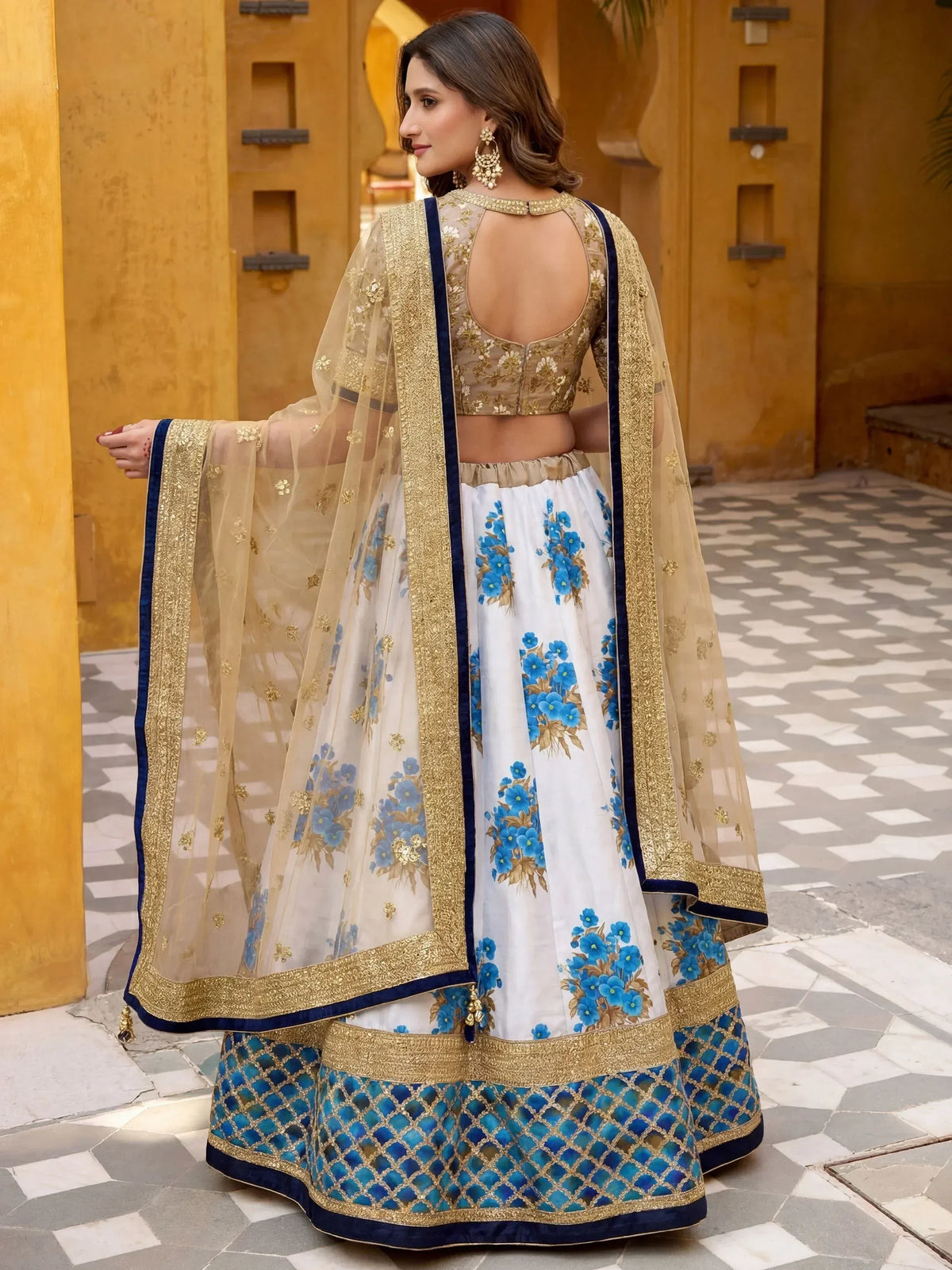 White lehenga with blue floral print, gold embroidery, and navy border, paired with sheer dupatta for Indian ethnic wear