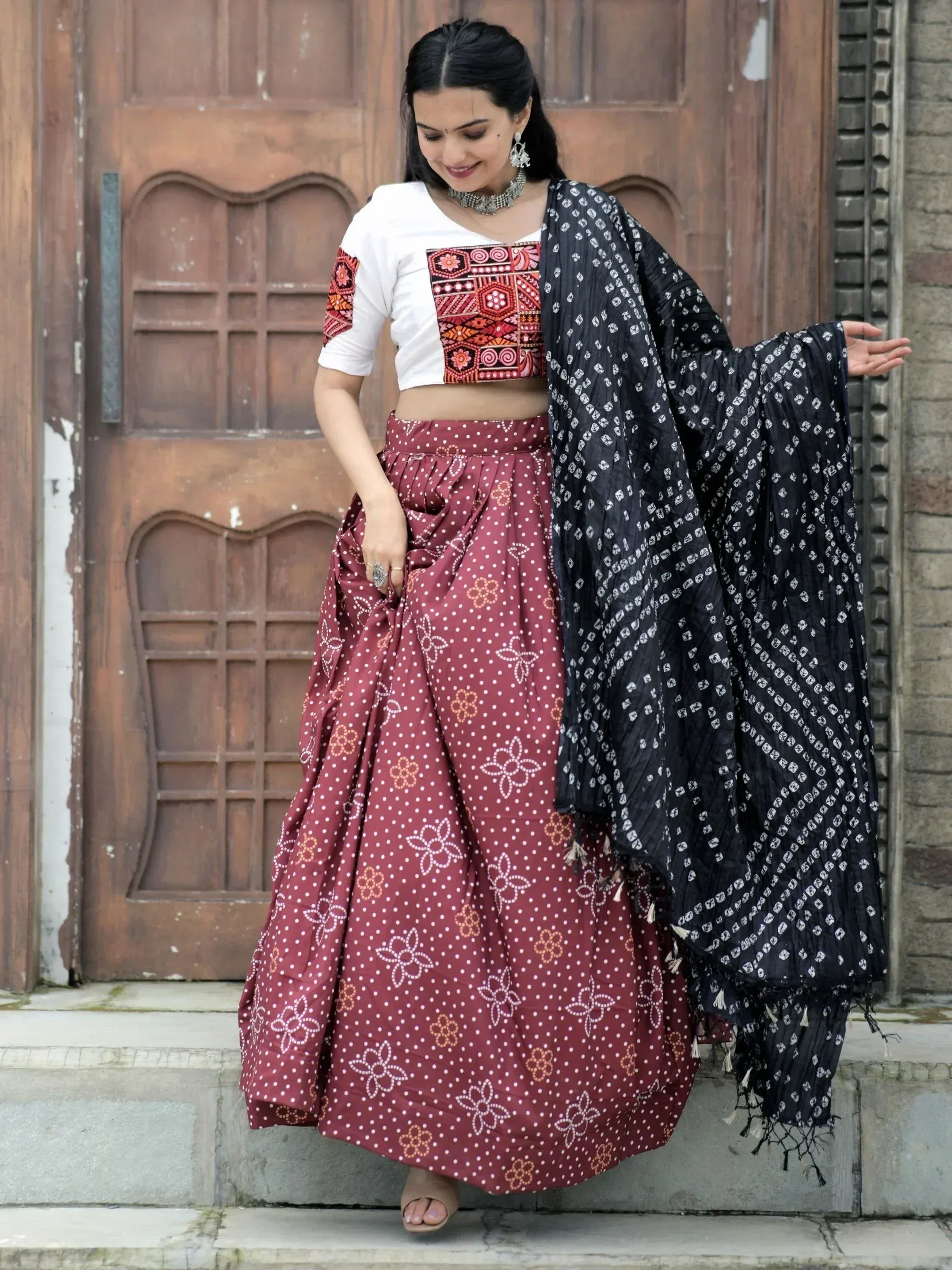 Woman in ethnic wear: embroidered crop top, maroon polka dot lehenga, black printed dupatta, traditional Indian outfit