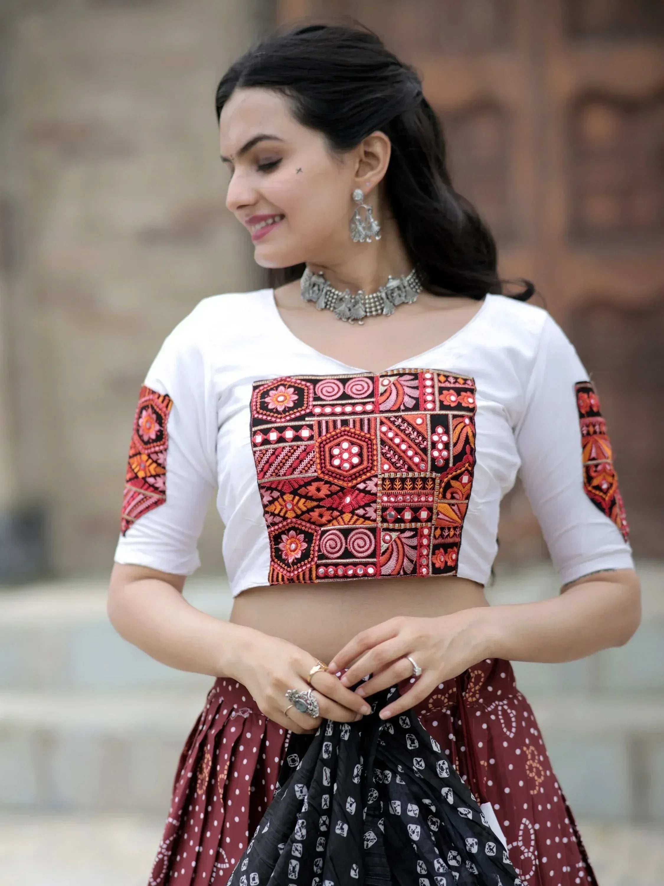 Woman in white crop top with colorful ethnic embroidery, paired with printed skirt, traditional jewelry