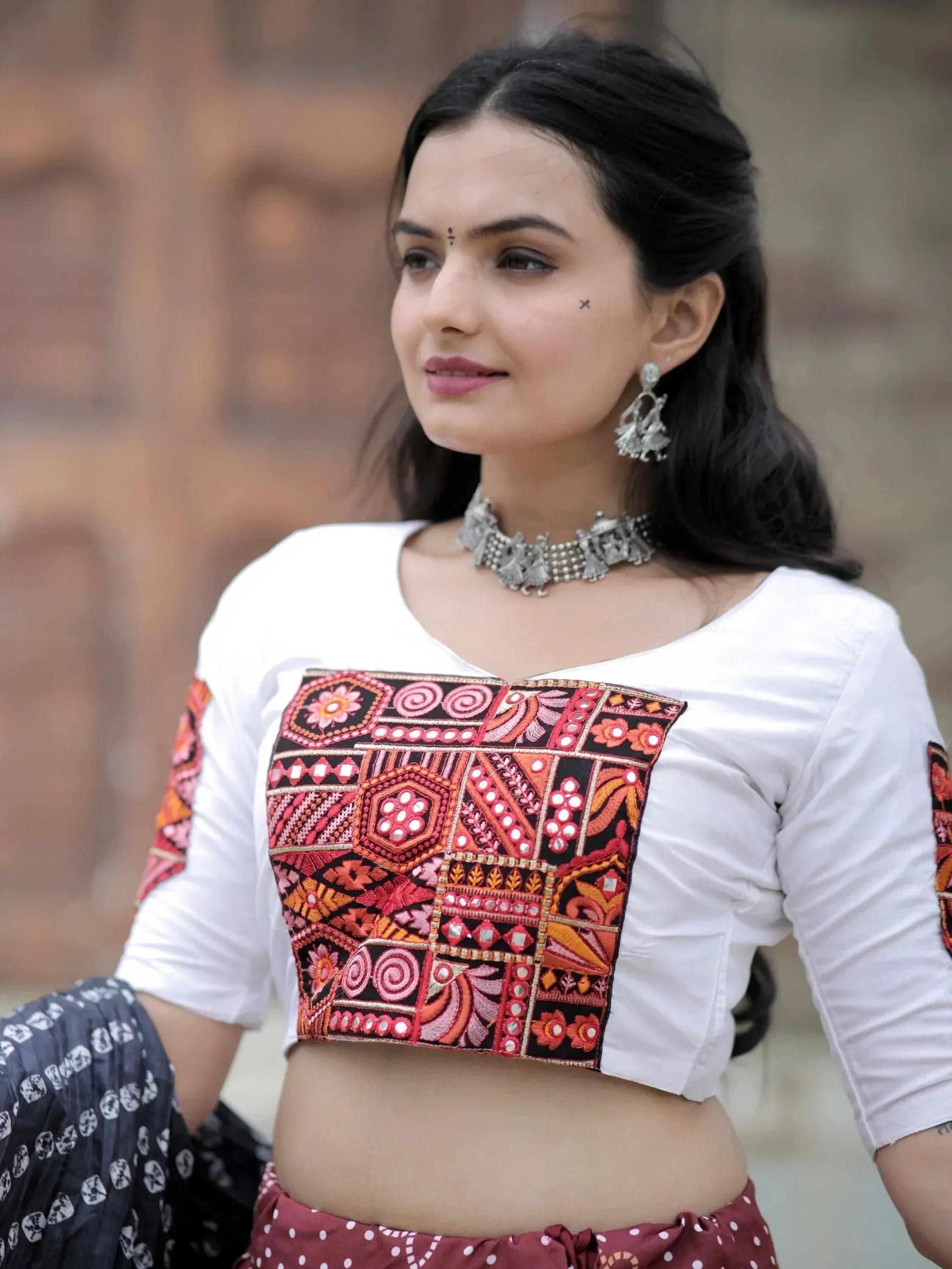 Woman in white crop top with colorful embroidered panel, ethnic jewelry, and polka dot skirt
