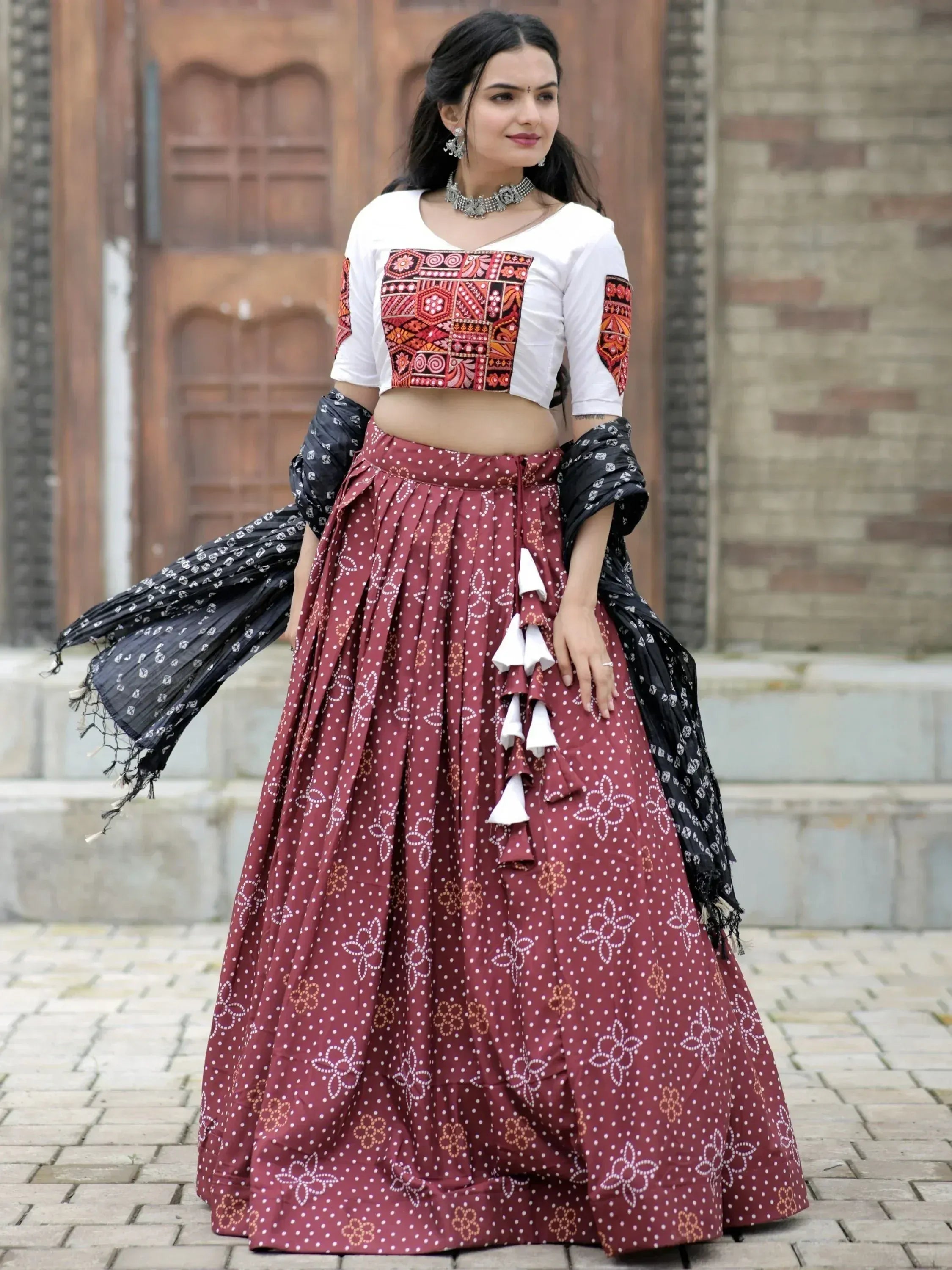 Woman in maroon printed lehenga with embroidered white crop top and black dupatta, ethnic Indian wear