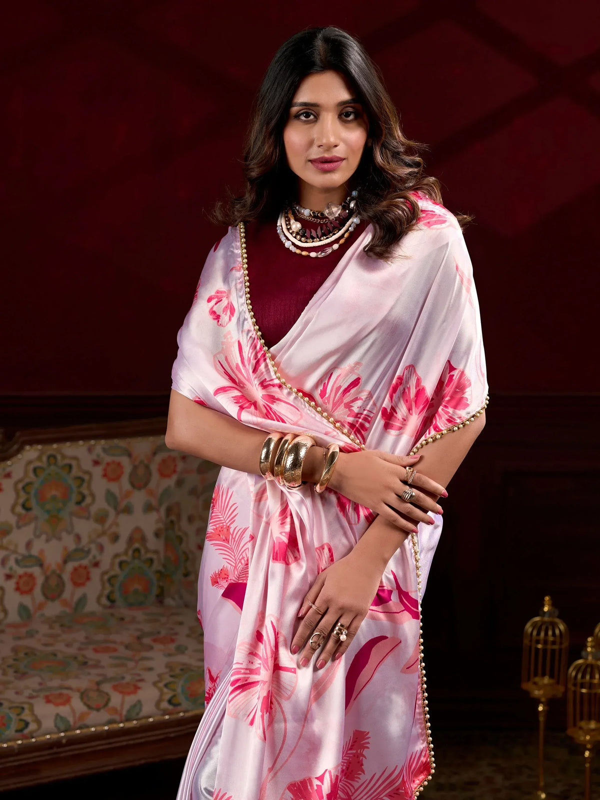 Woman in pink floral saree with pearl border, styled with gold jewelry for ethnic occasions