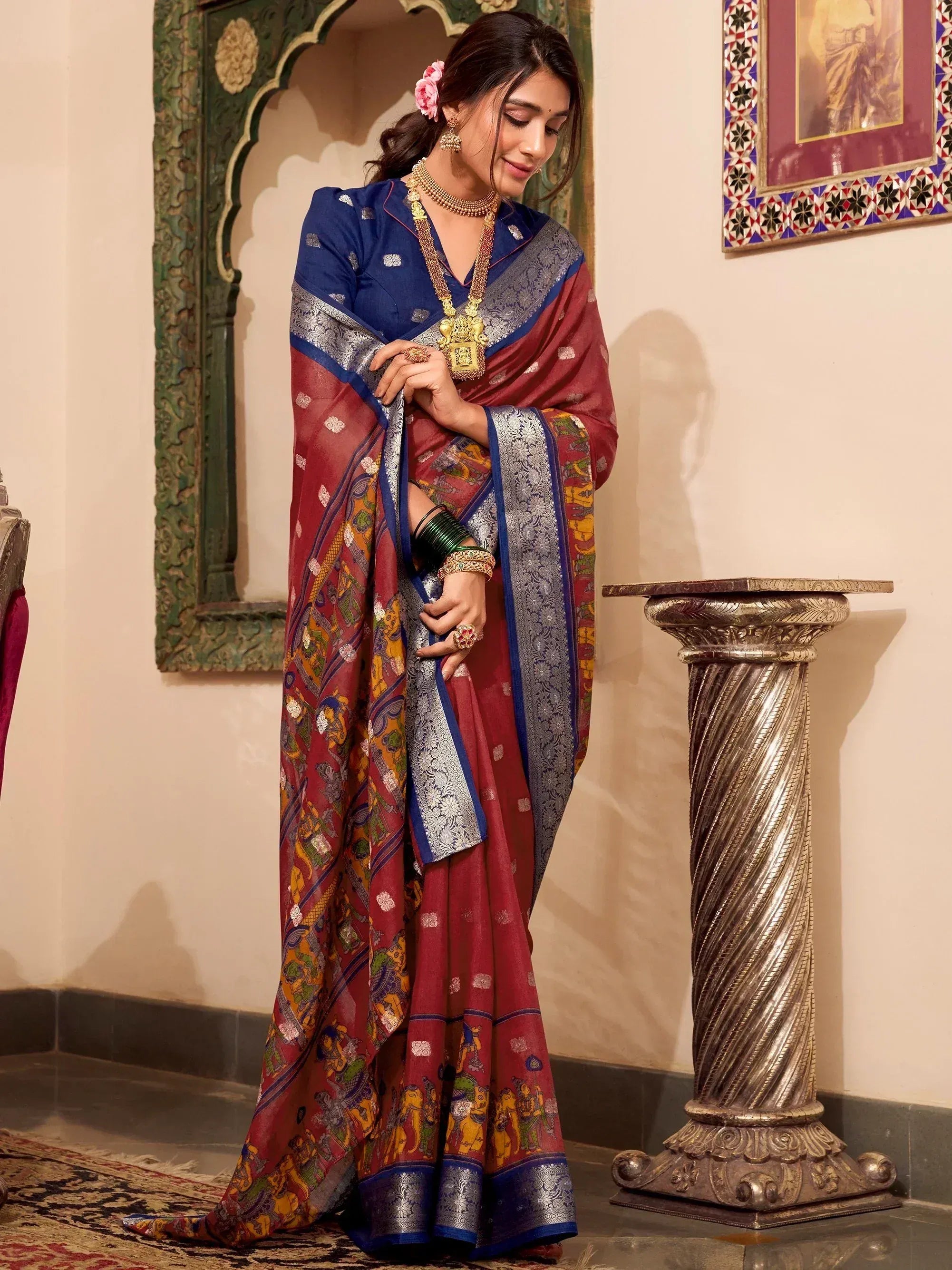 Elegant maroon and blue saree with intricate elephant print and silver border, paired with gold jewelry.