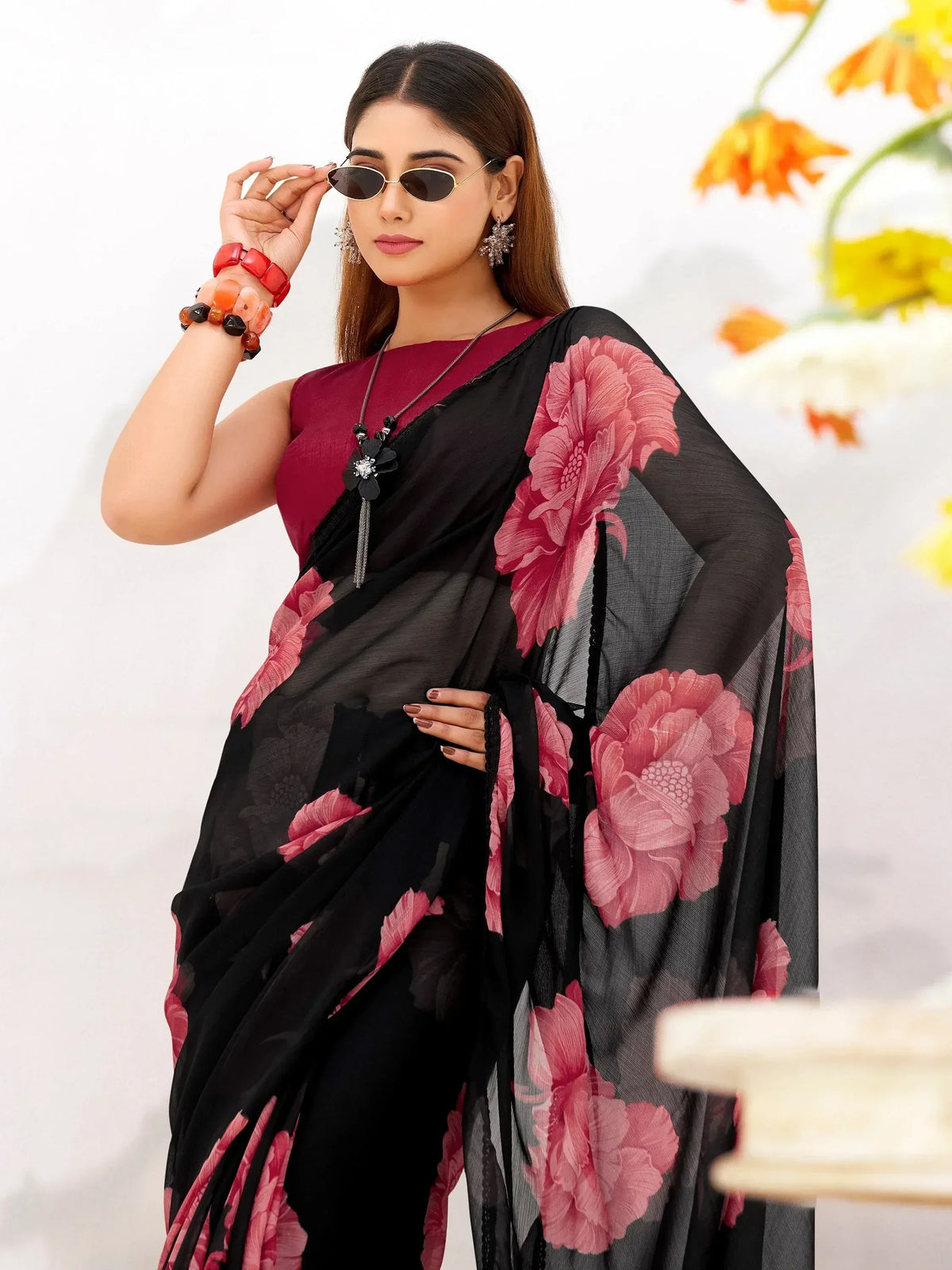 Woman in black saree with pink floral print, maroon blouse, sunglasses, and statement jewelry