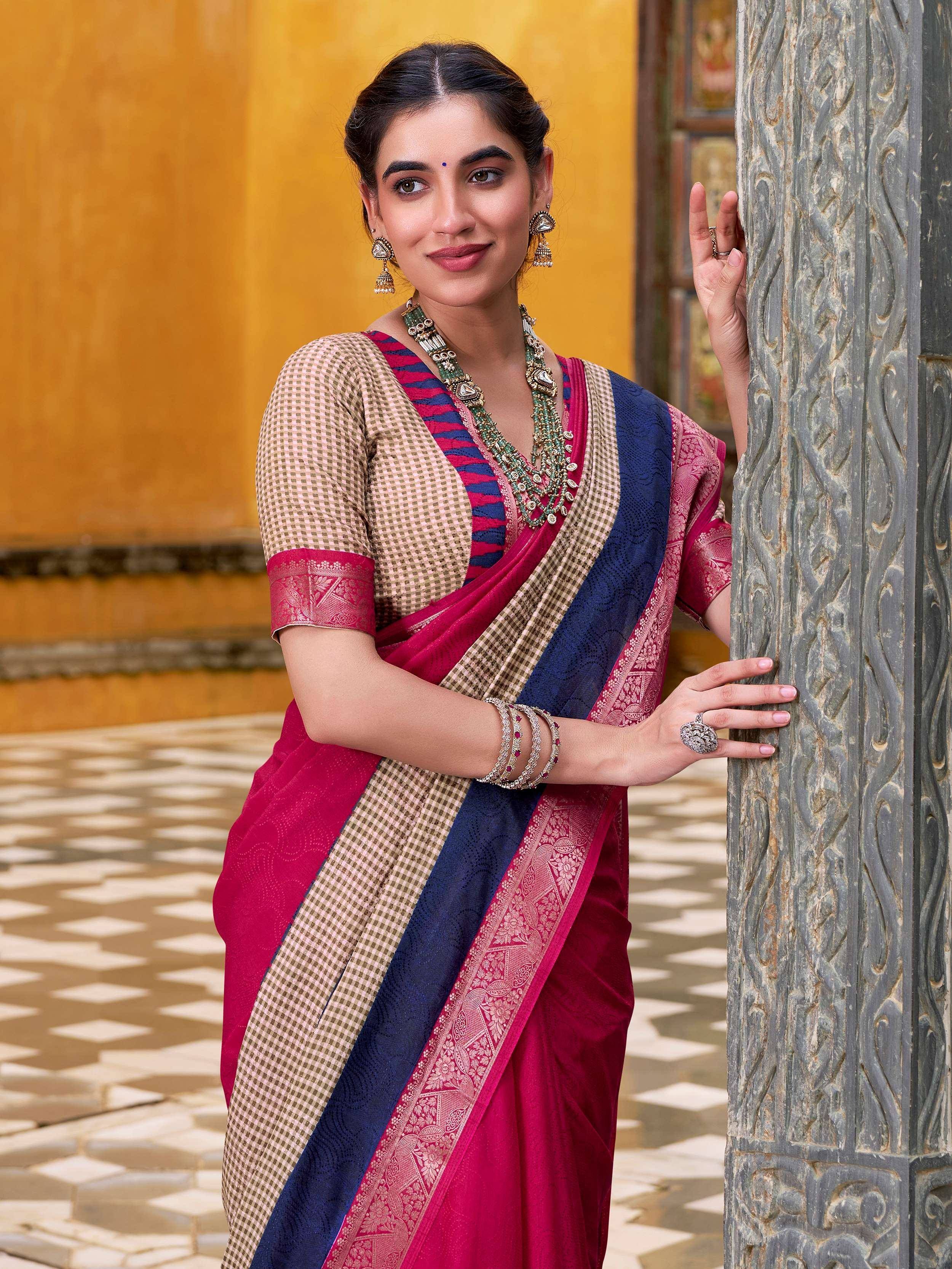 Woman in vibrant pink and blue ethnic saree with checkered blouse, traditional jewelry, leaning on carved pillar