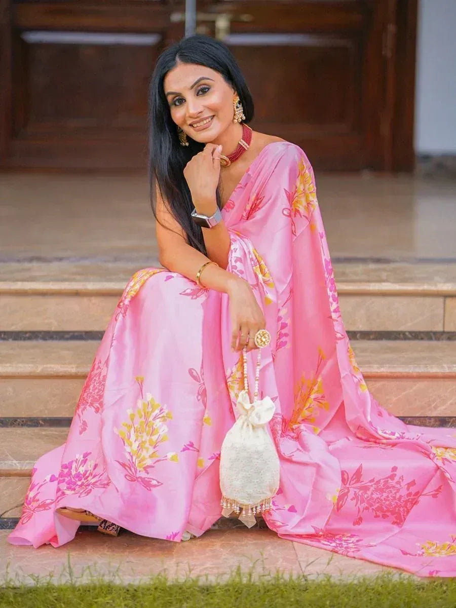 Woman in pink floral ethnic gown with matching dupatta, gold jewelry, and potli bag, seated on steps